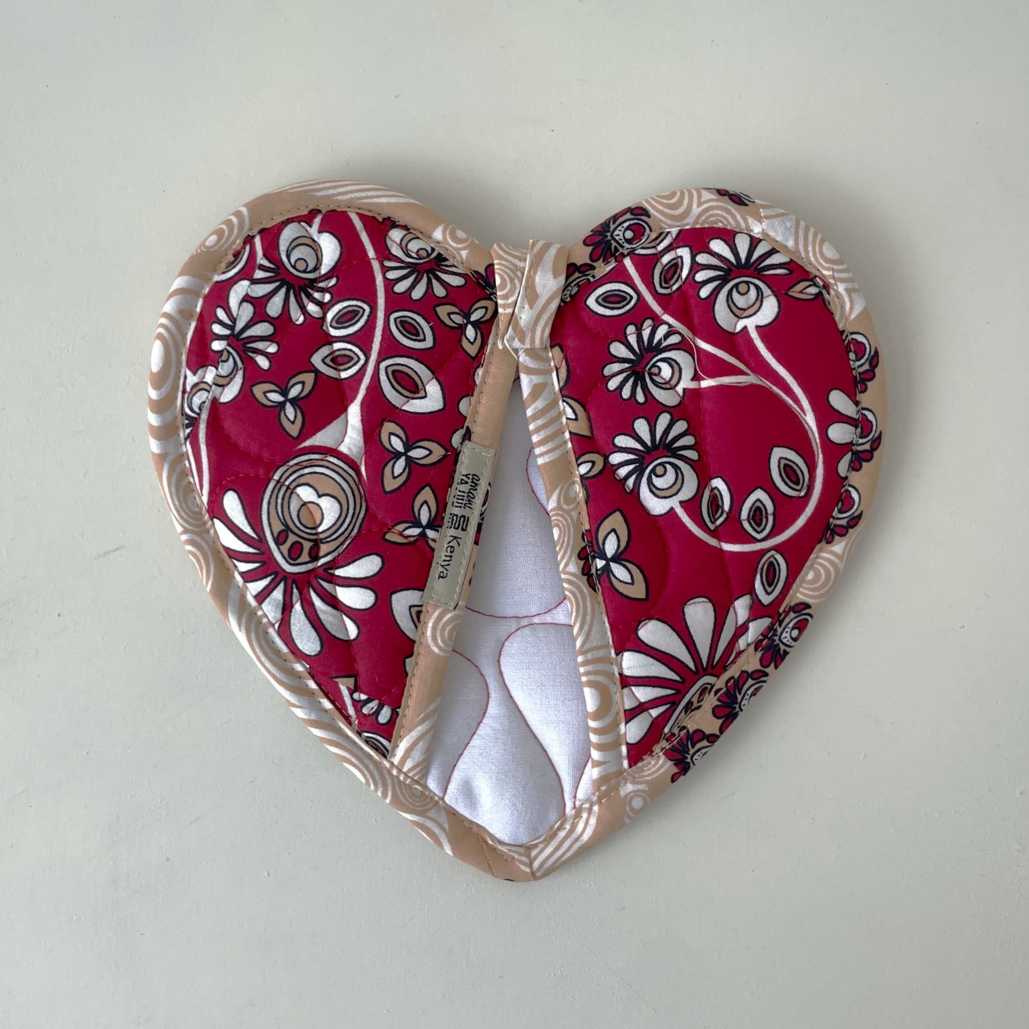 Heart-shaped hot pad with red and white floral pattern on a light gray background
