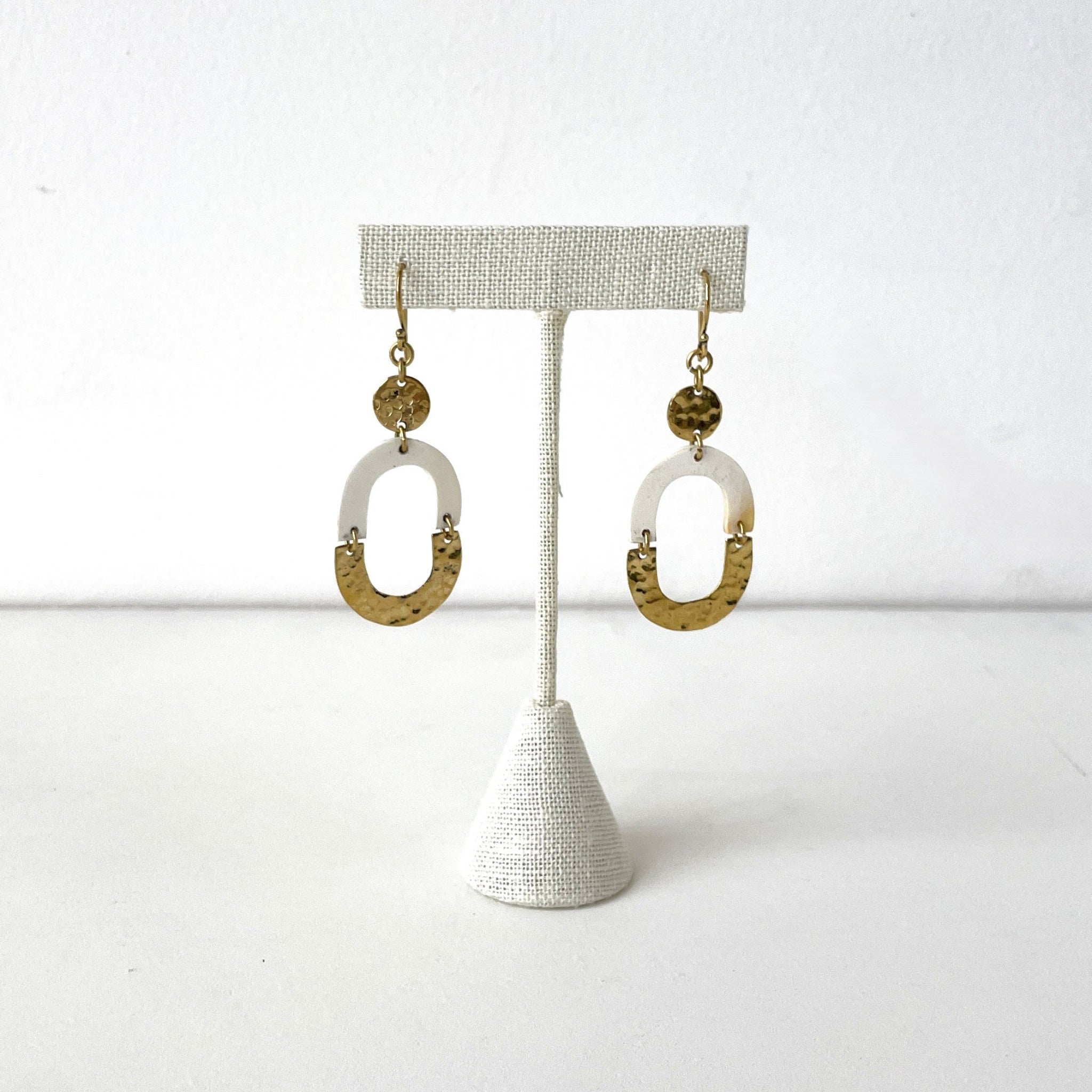 Pair of gold and white earrings on a textured stand against a white background