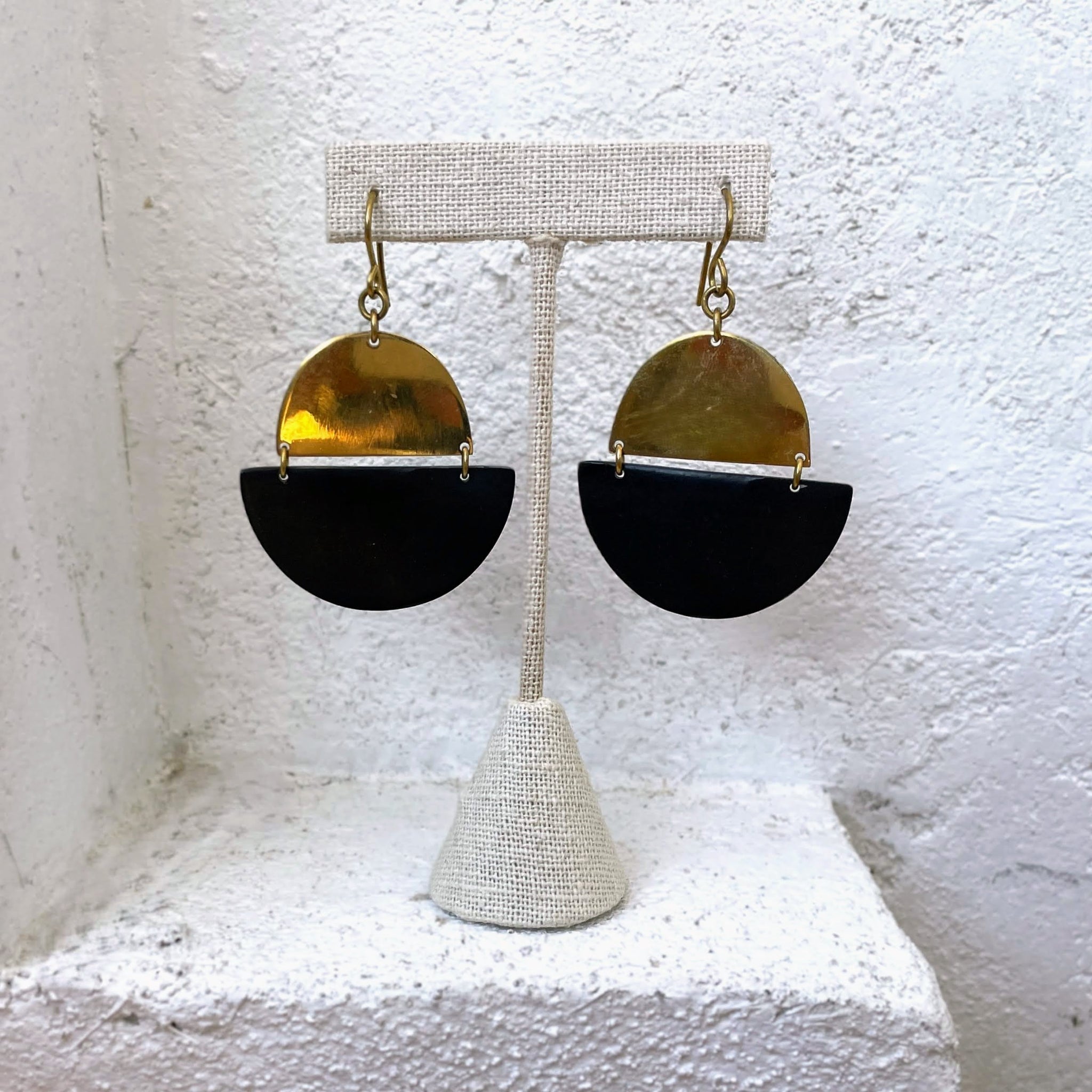 Brass and black horn half-circle earrings on a stand against a textured white background