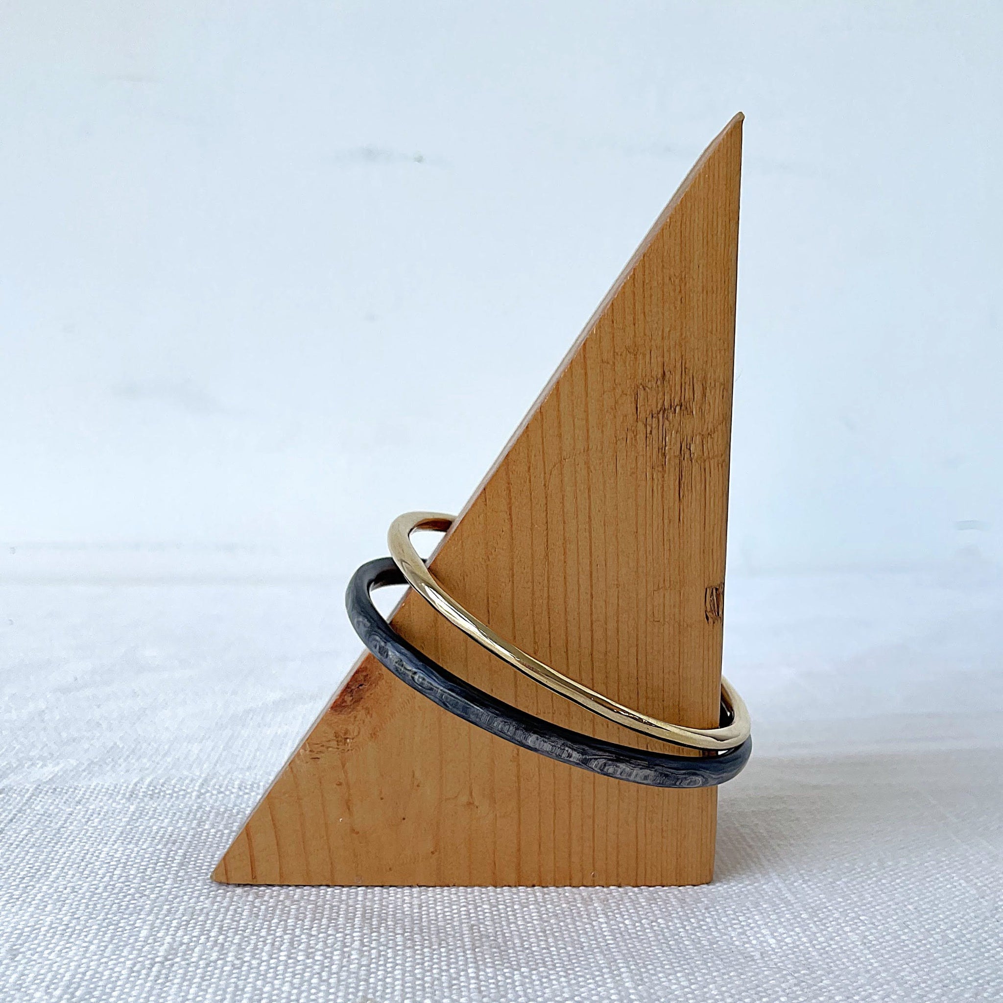 Wooden triangle-shaped stand with brass and horn bracelets on a white background