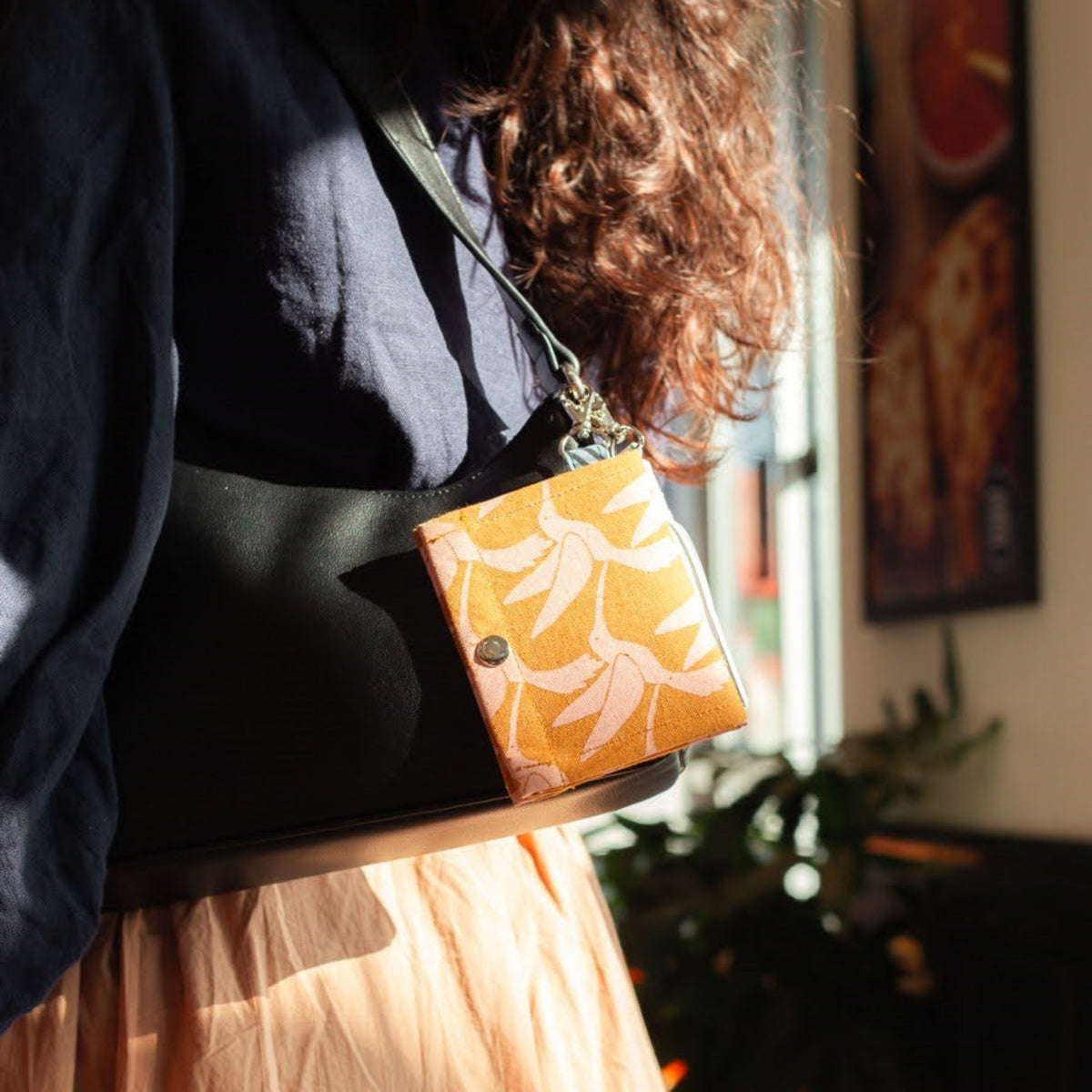 Person holding a black bag with a bird patterned ID wallet indoors