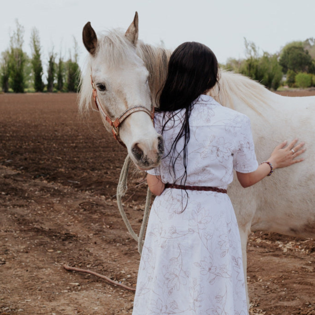A person standing next to a white horse, wearing a white Magnolia Dress 