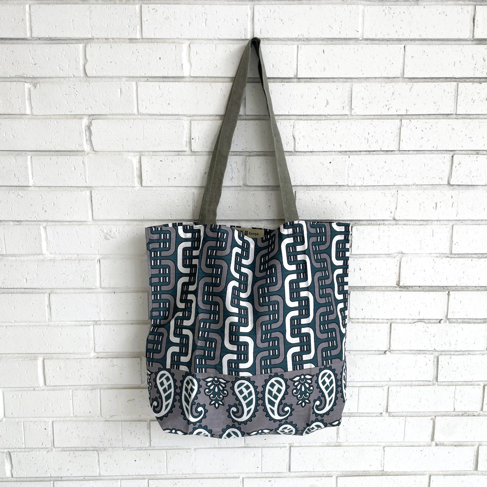 Tote bag with a geometric pattern hanging against a white brick wall.