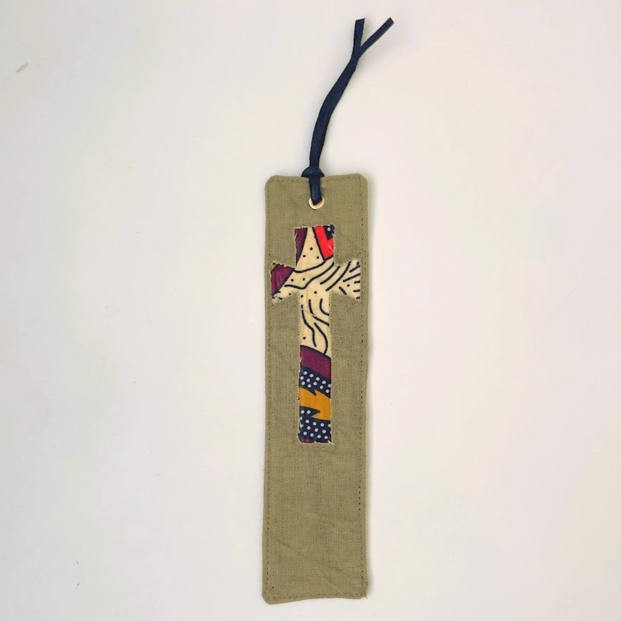 A fabric bookmark with a long rectangular body in an olive color and a small cross patchwork design in the center. The bookmark has a dark navy blue hanging loop at the top and is photographed against a plain off-white background.