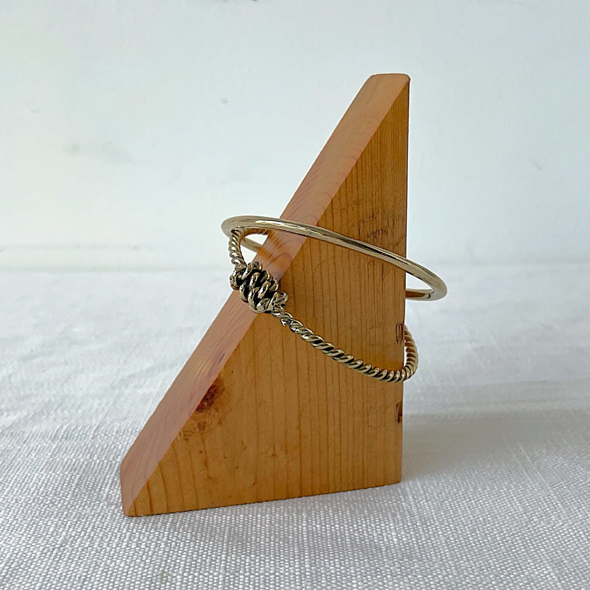 Wooden triangle-shaped jewelry holder with a brass bangle set on a white background