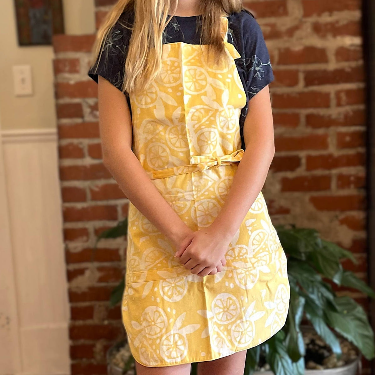 Person wearing a yellow apron with lemon pattern in front of a brick wall.