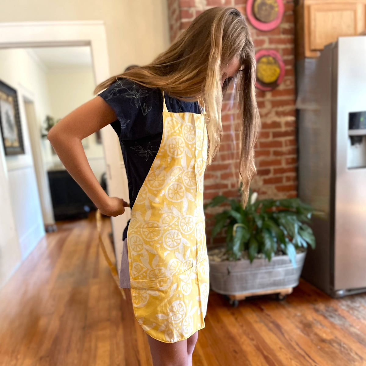 Woman wearing a yellow apron with a black top in a kitchen.