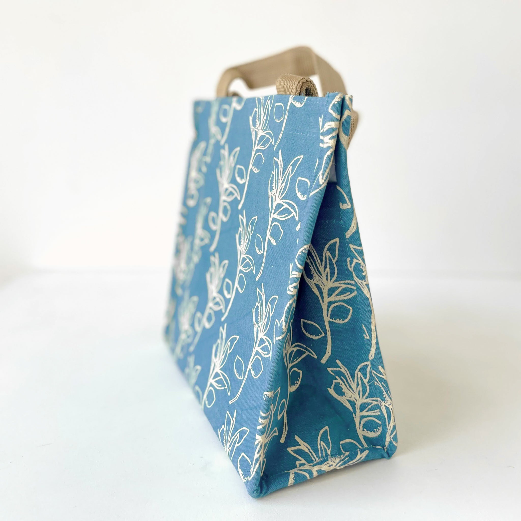 A blue fabric lunch tote bag with a cream olive leaf pattern and natural beige canvas handles, shown against a plain white background.