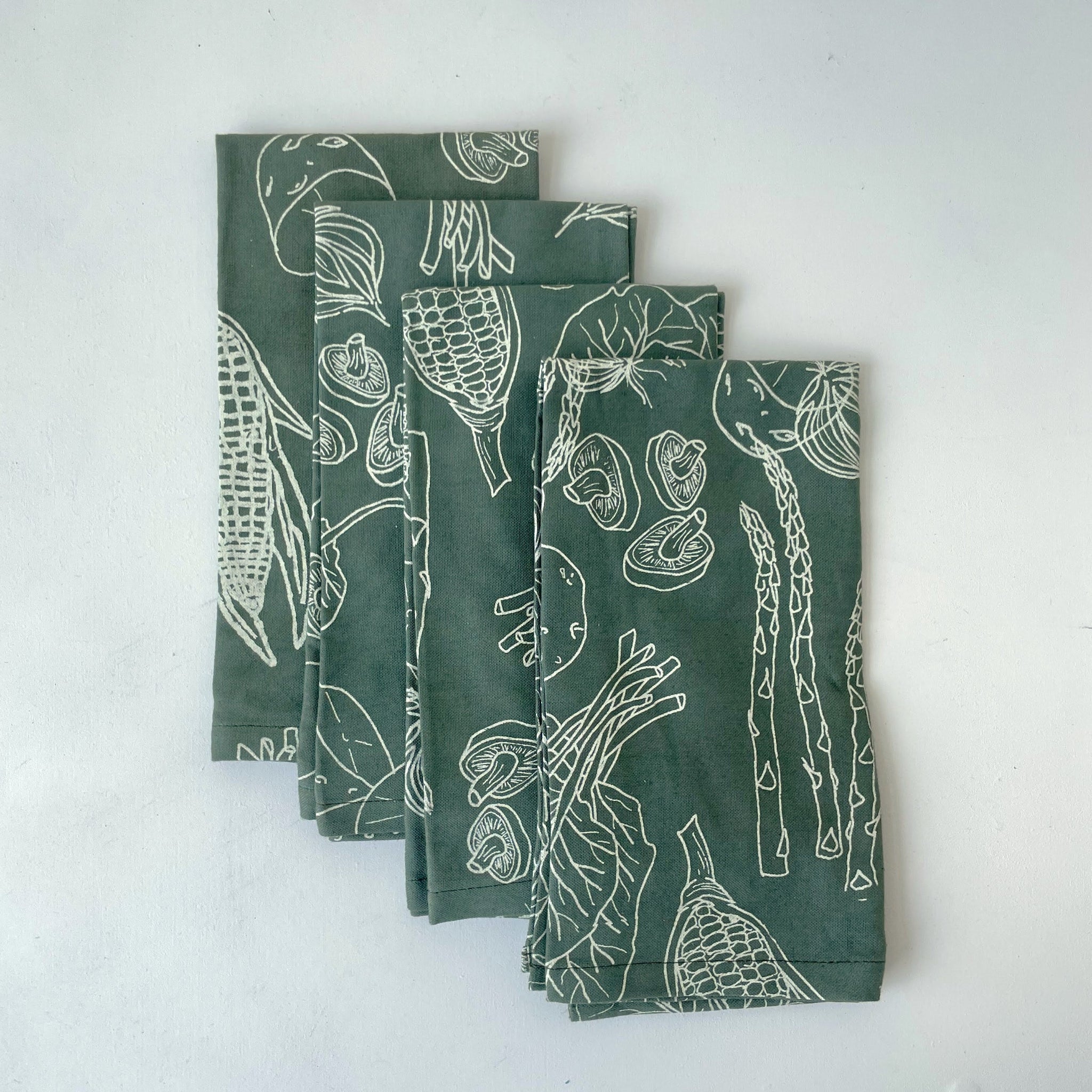 Set of four green napkins with white line vegetable drawings on a white background