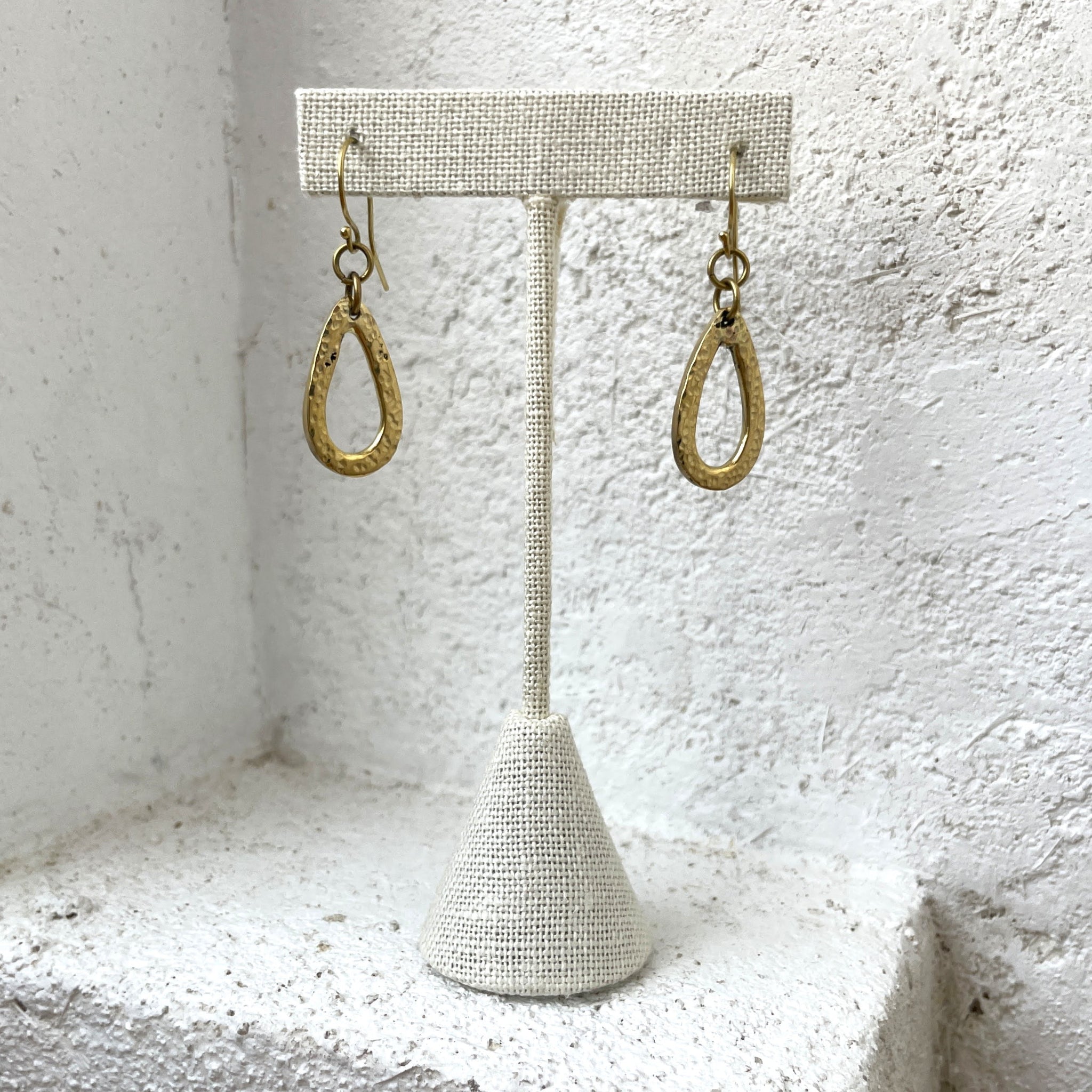 Gold hoop earrings on a textured white stand against a textured white background