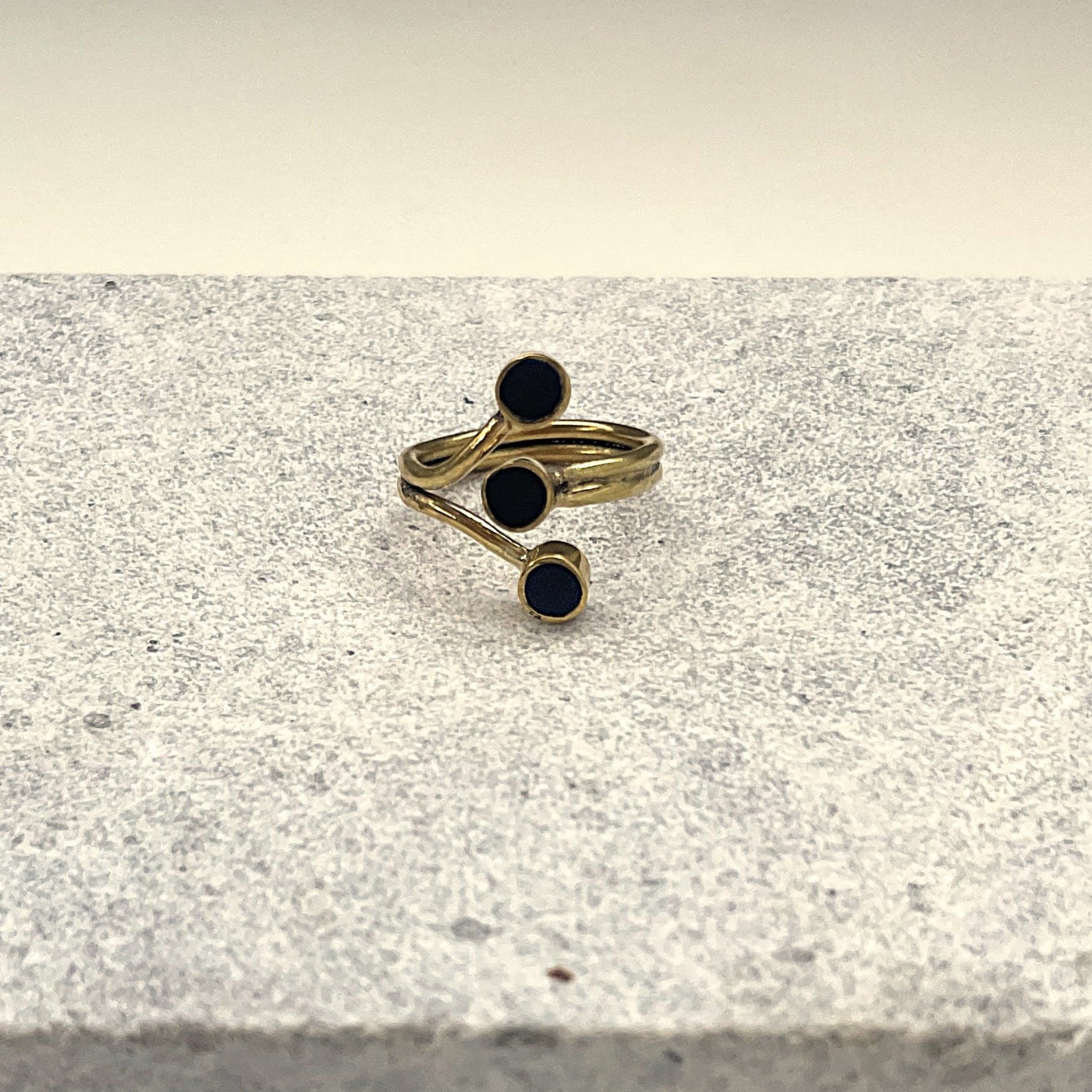 Adjustable brass and black horn discs ring on a stone surface