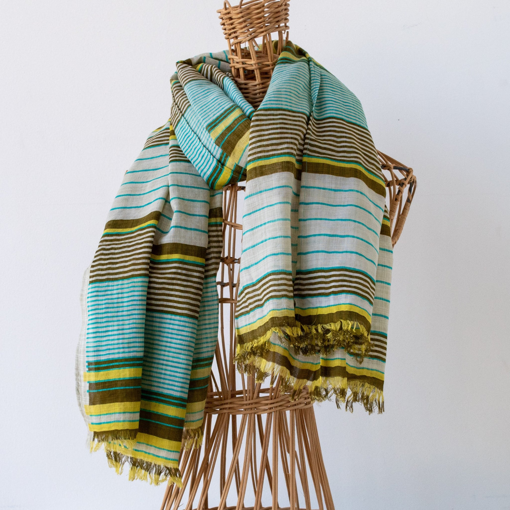 A striped woven scarf with fringed edges draped over a wicker mannequin torso against a plain white background.
