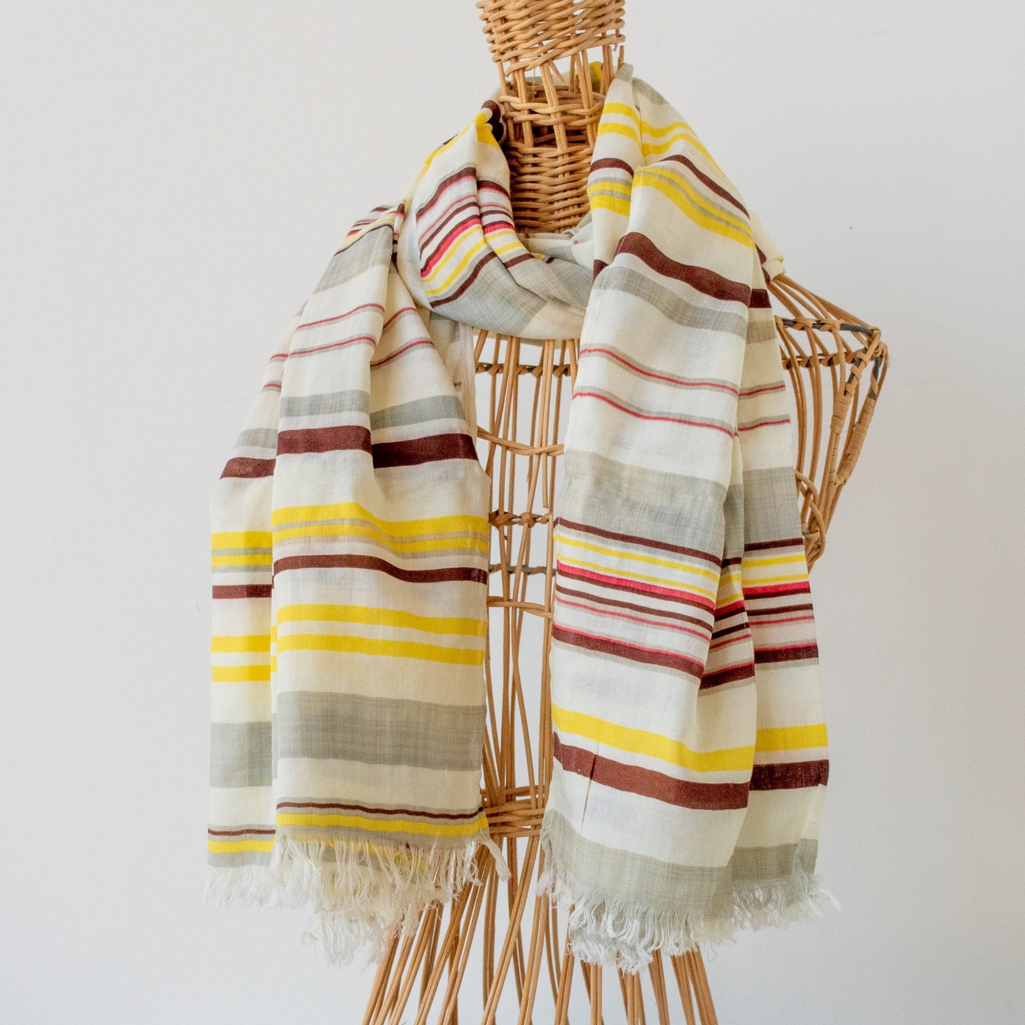 A striped woven scarf with fringed edges draped over a wicker mannequin torso against a plain white background.
