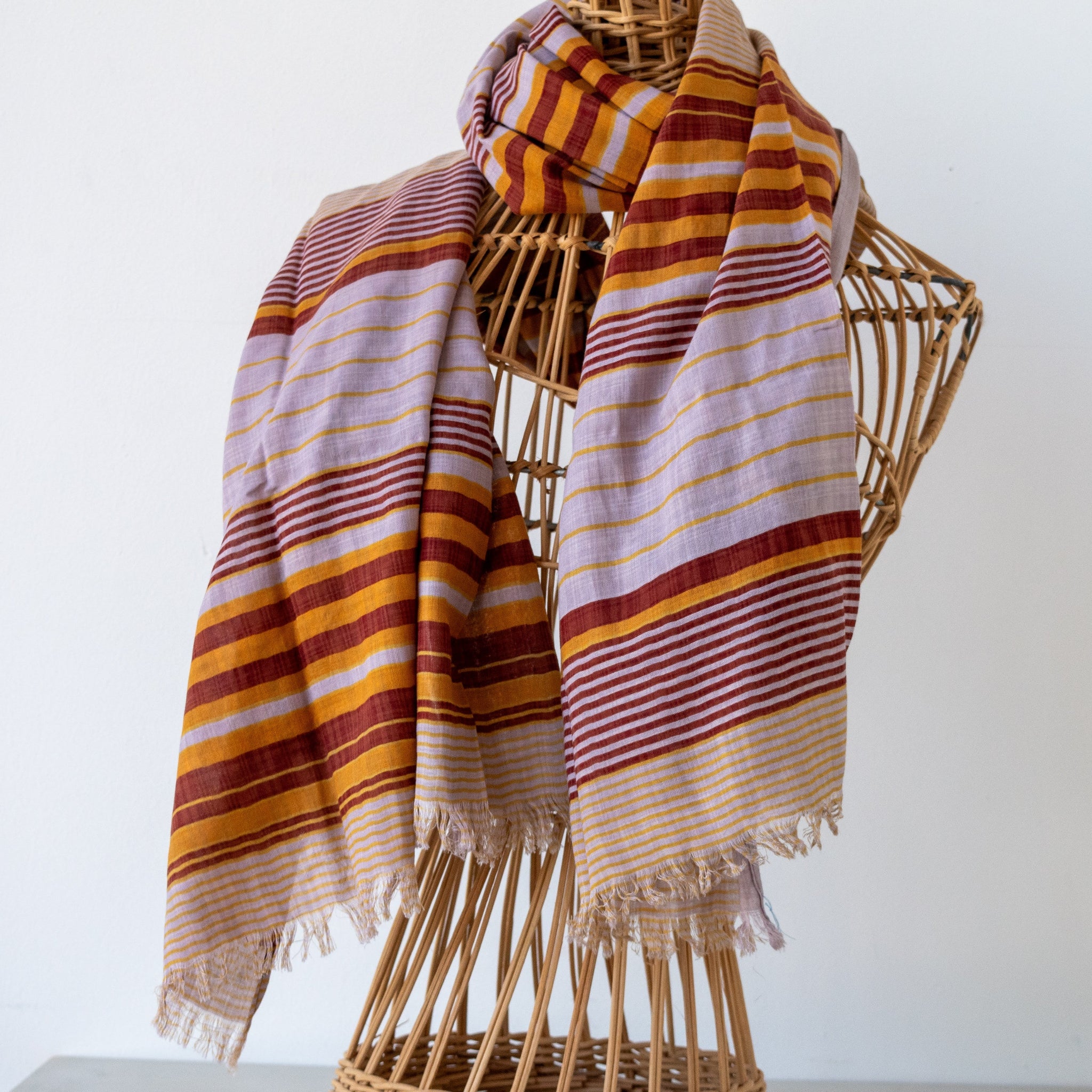 A striped woven scarf draped over a wicker mannequin torso against a plain light background.