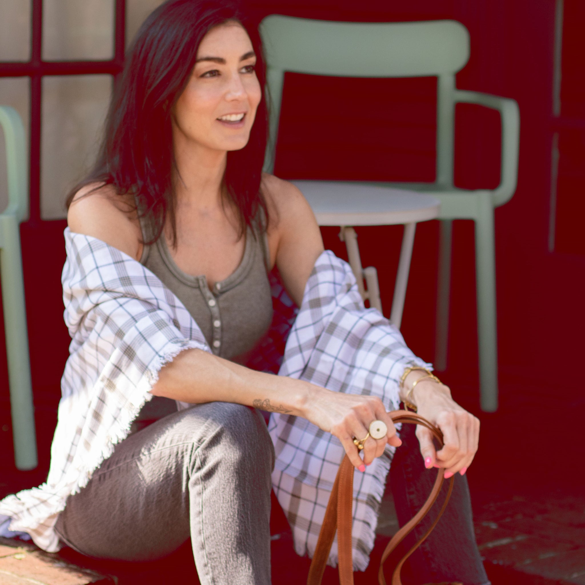 Woman sitting on a red chair with a plaid shawl, holding a brown leather bag.