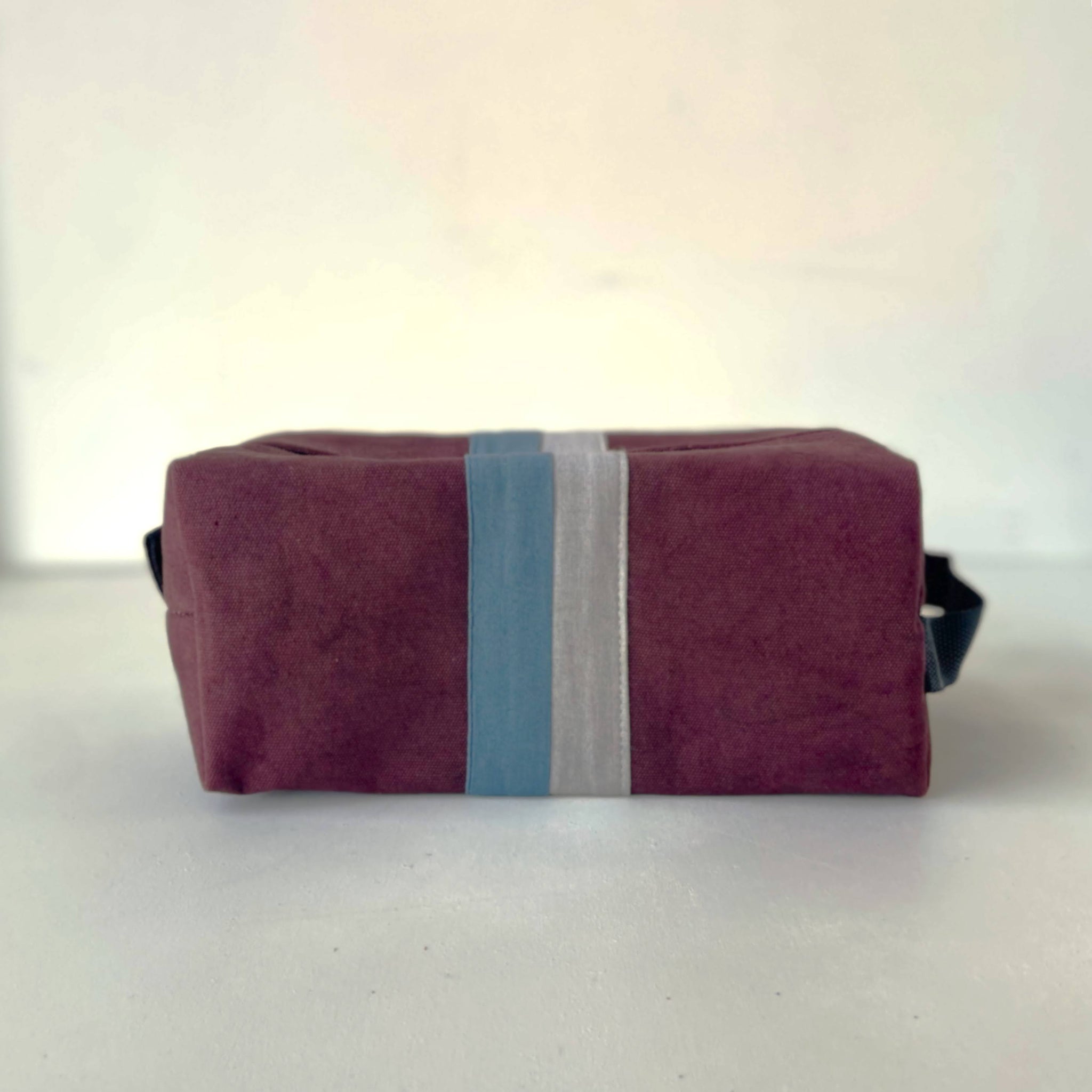 Plum pouch with blue and gray stripes on a white background