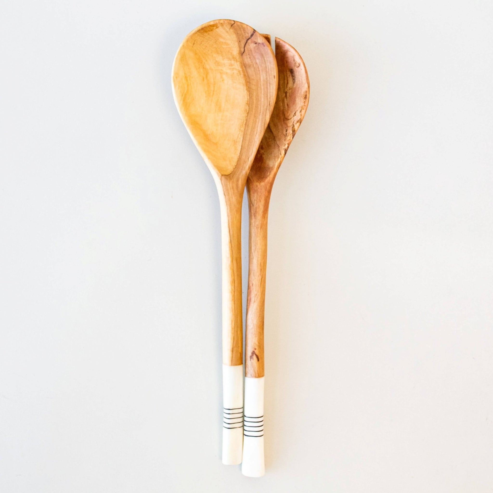 Two wooden spoons with white handles on a light gray background