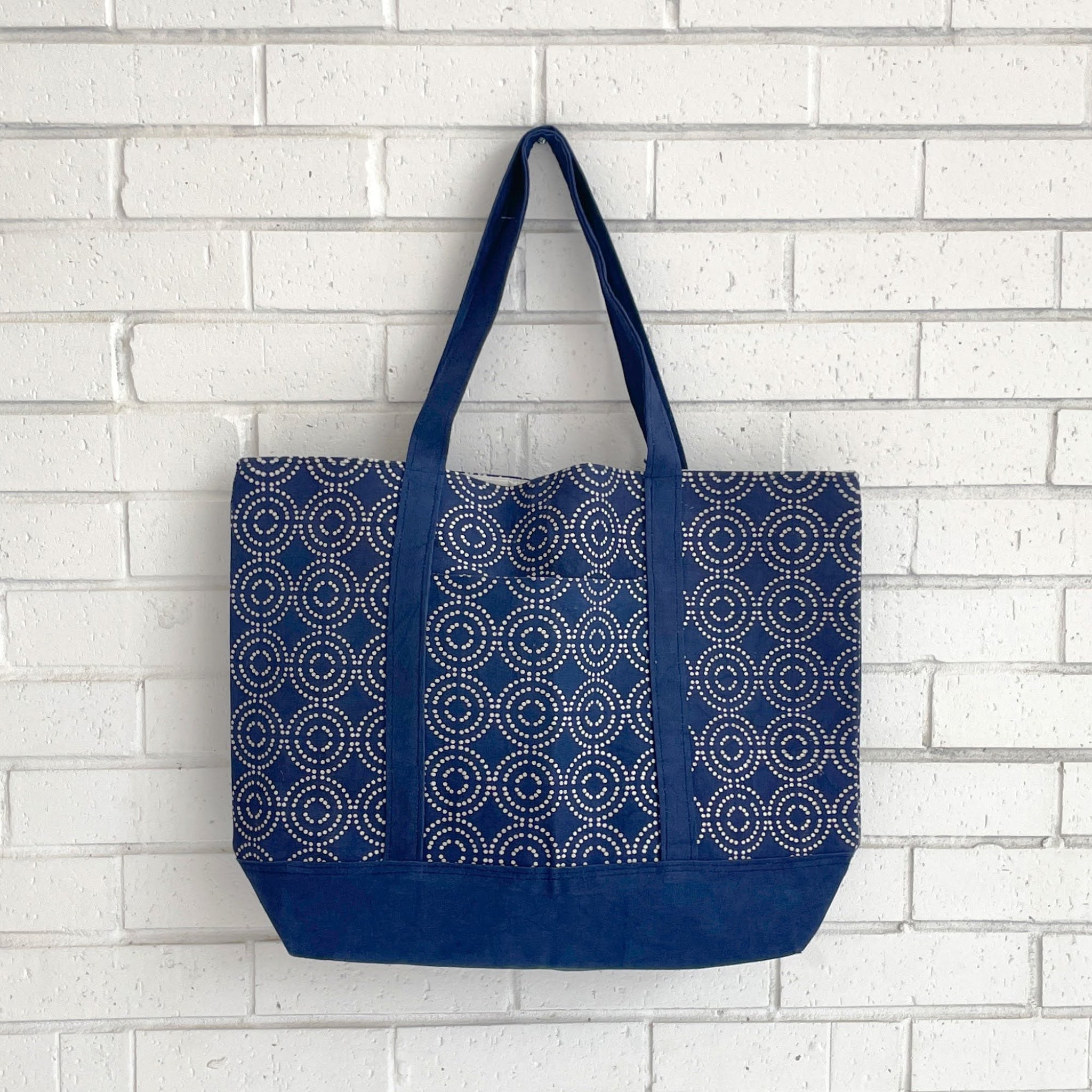 Blue tote bag with circular pattern against a white brick wall