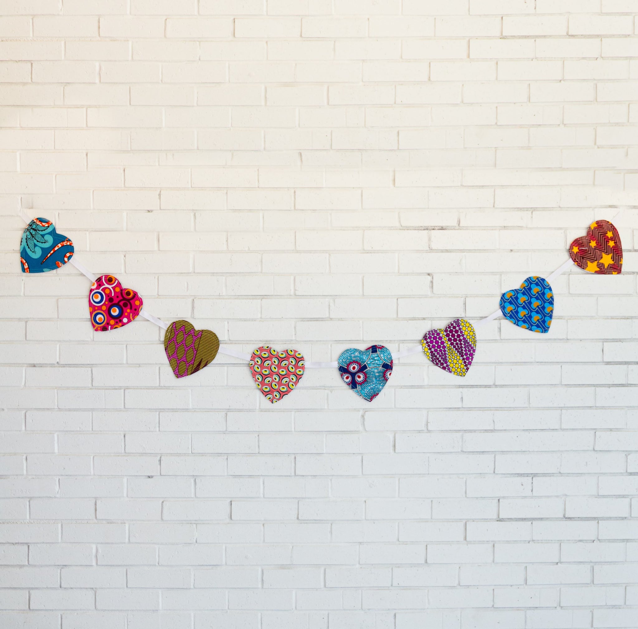 Multi-colored heart garland in front of white brick wall
