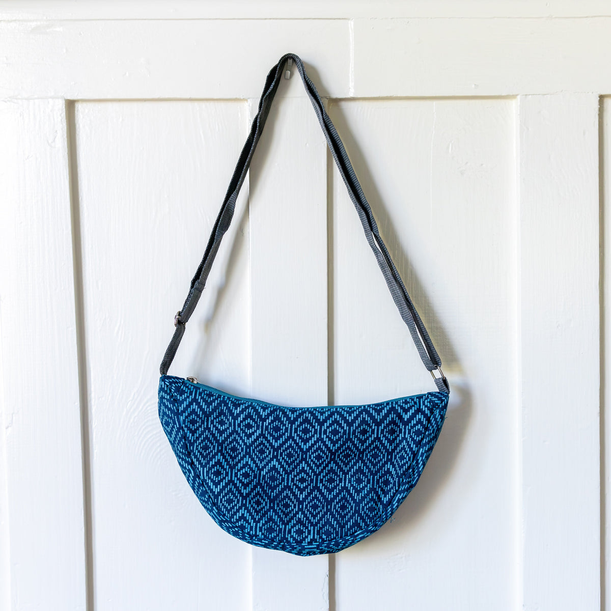 Teal basket weave pattern crescent sling bag hanging from a white door