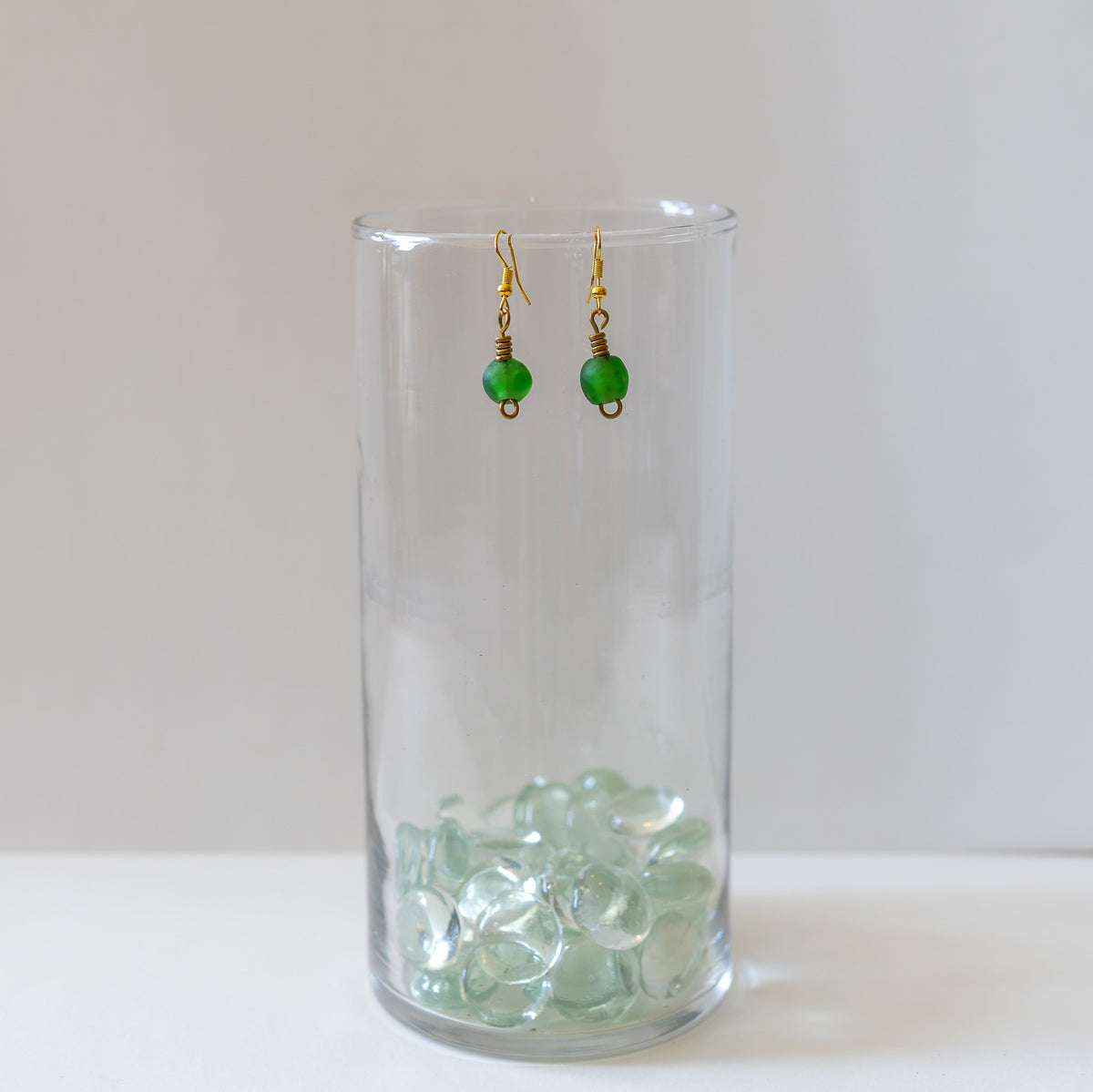 Green bottle bead and brass earrings hanging from a clear glass