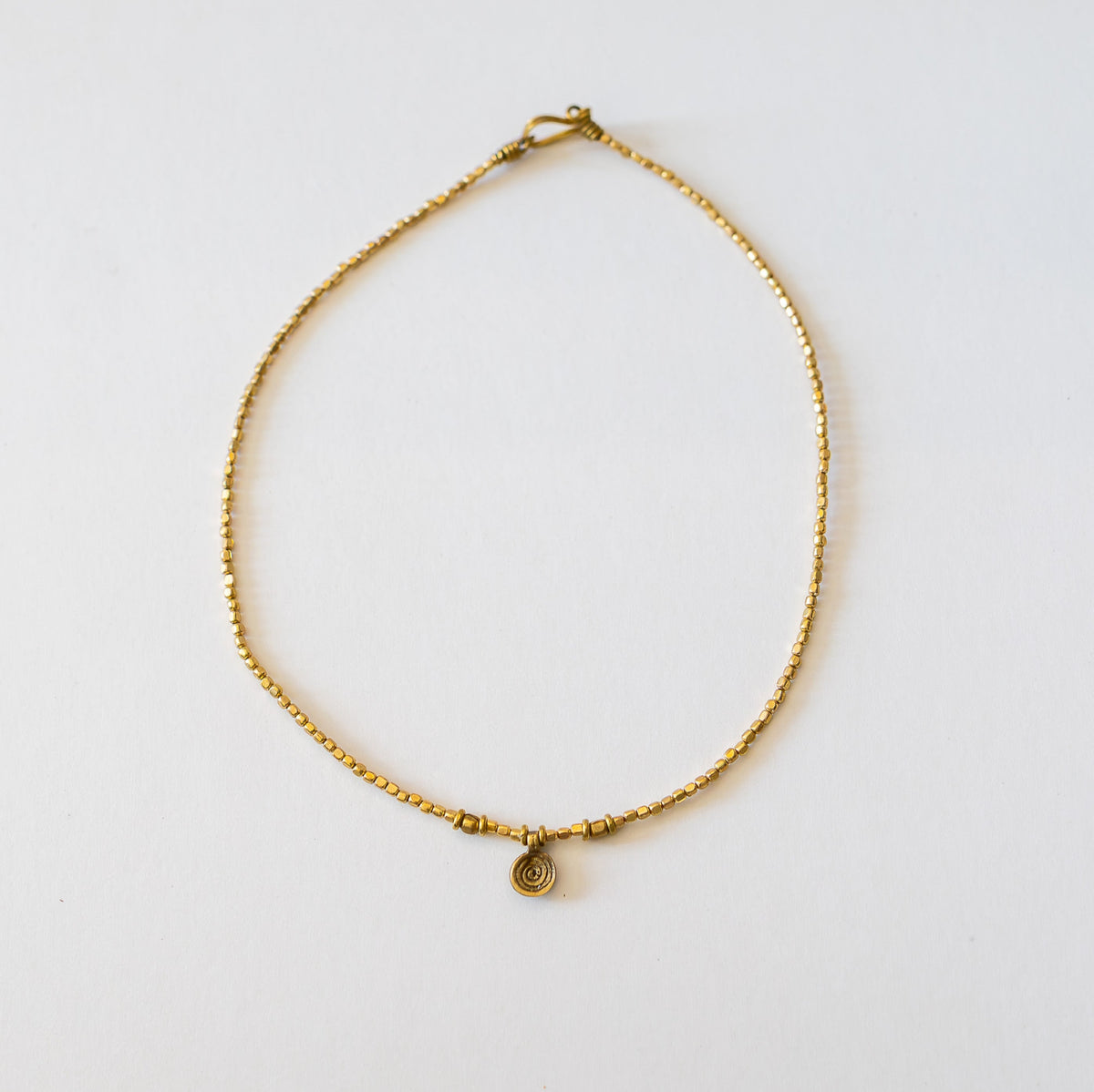 Small swirl brass pendant necklace with hook closure on white background