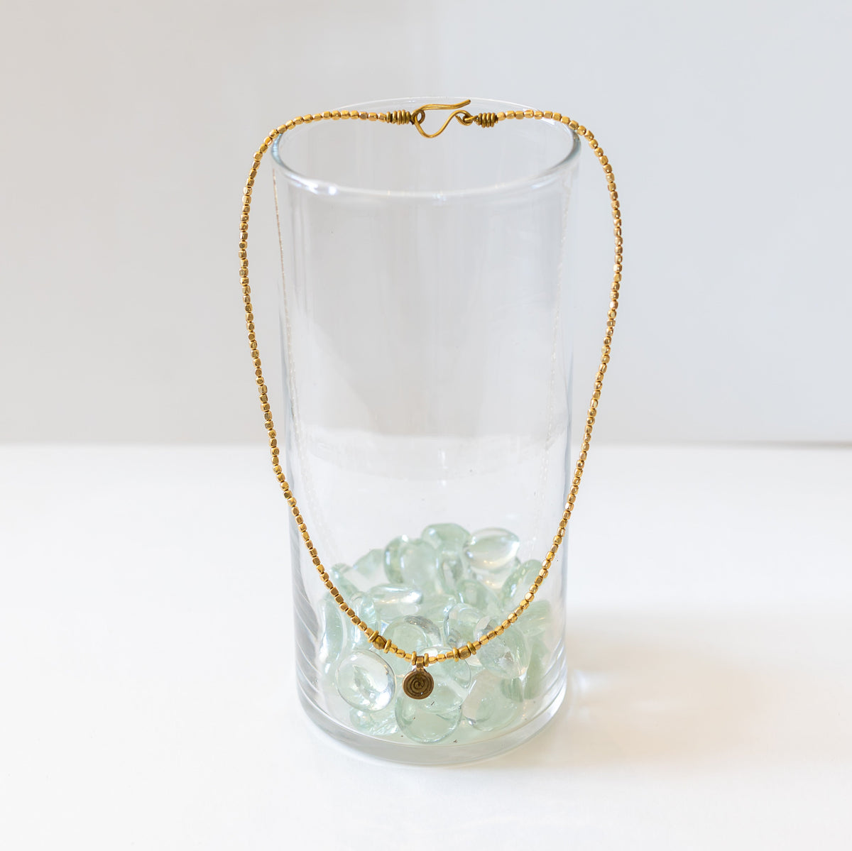 Small swirl brass pendant with hook closure hanging on a clear glass
