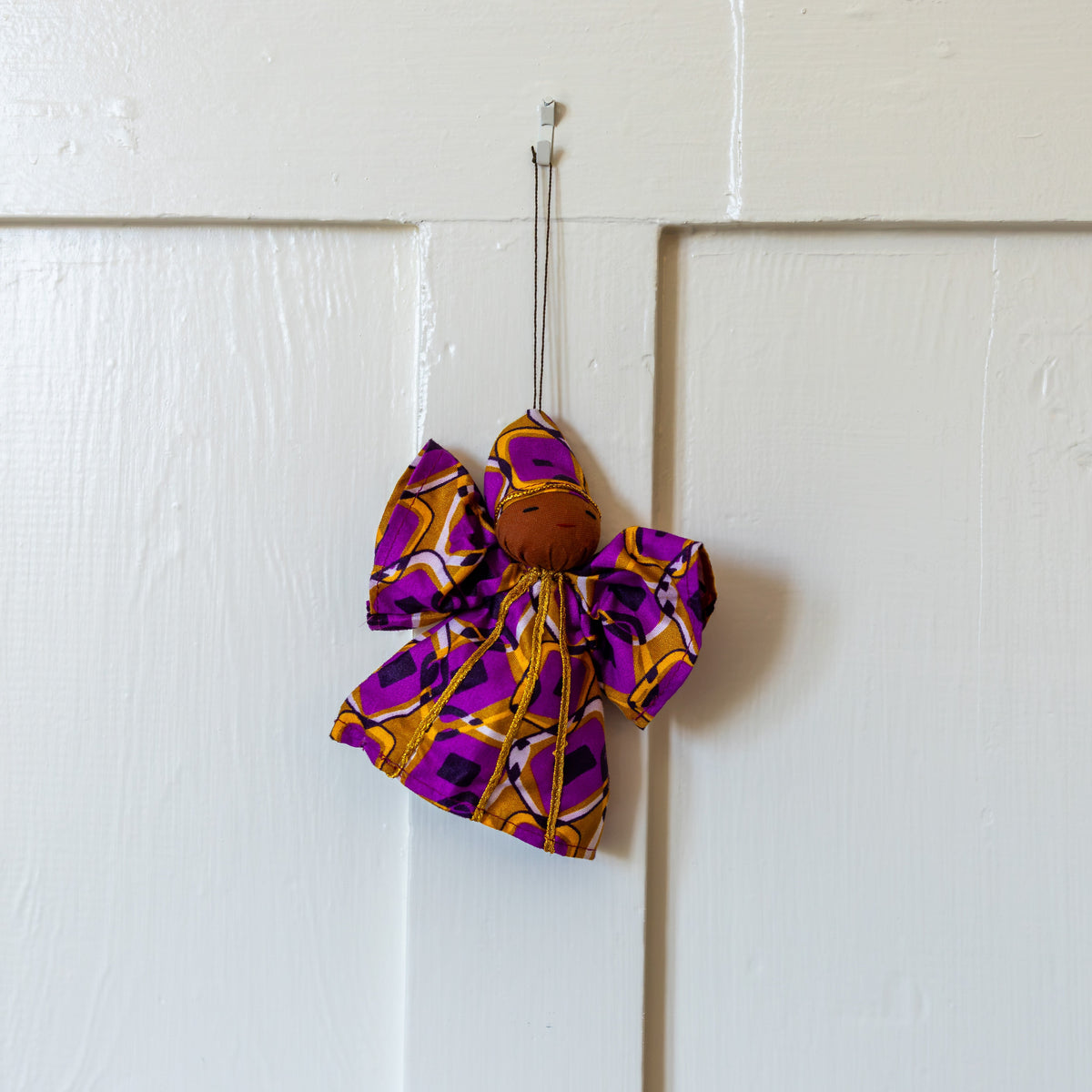 Purple and gold fabric peace angel ornament hanging on a white door