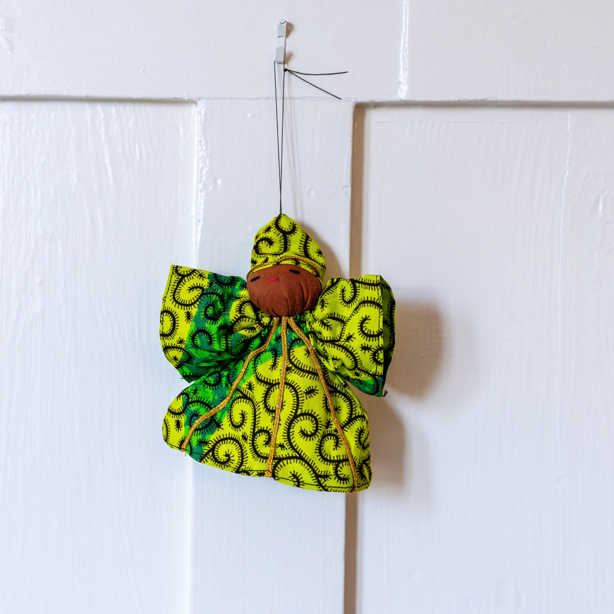 Green and gold fabric peace angel ornament hanging on a white door
