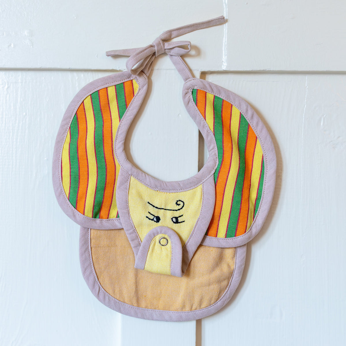 Yellow, green, pink, and orange striped elephant bib hanging on a white door