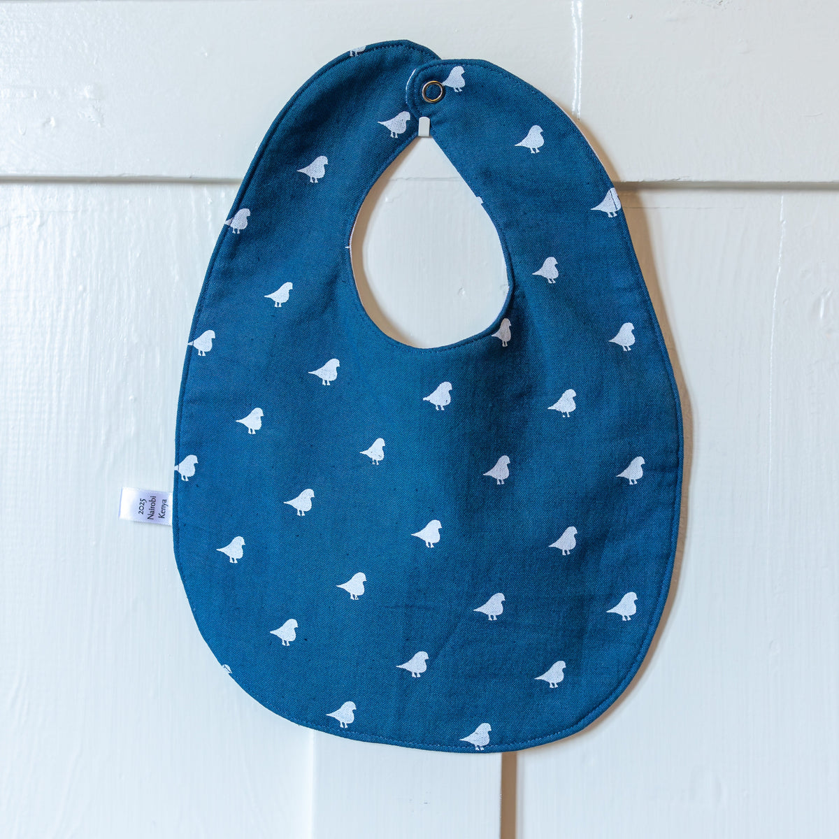 Blue baby bib with white birds hanging on a white door