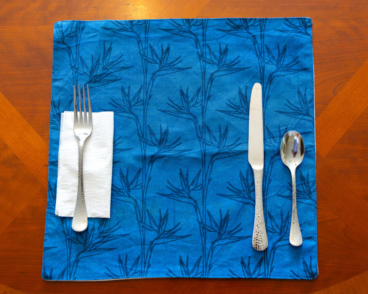 Blue placemat with bird of paradise pattern with white napkin and silverware on a wooden table