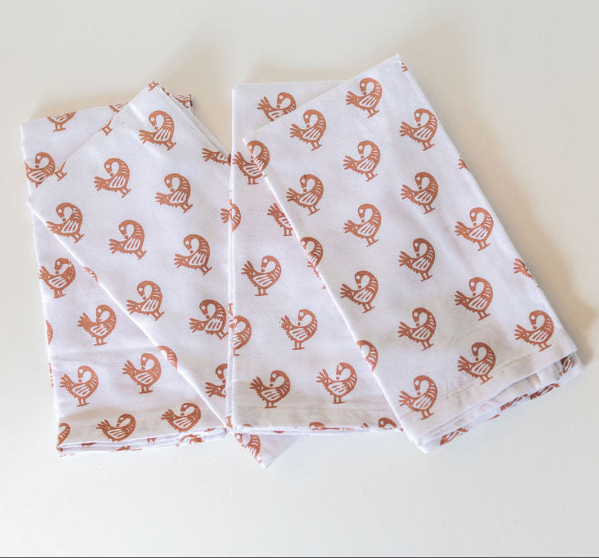 Set of white napkins with tan birds displayed on a white surface