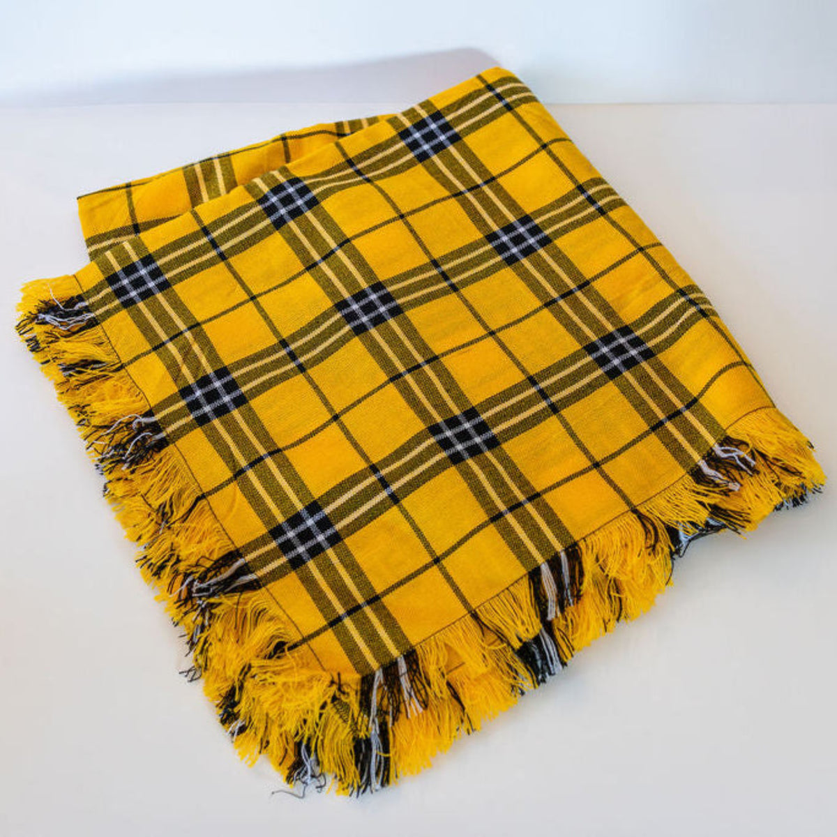 Folded gold and black plaid scarf on a white surface