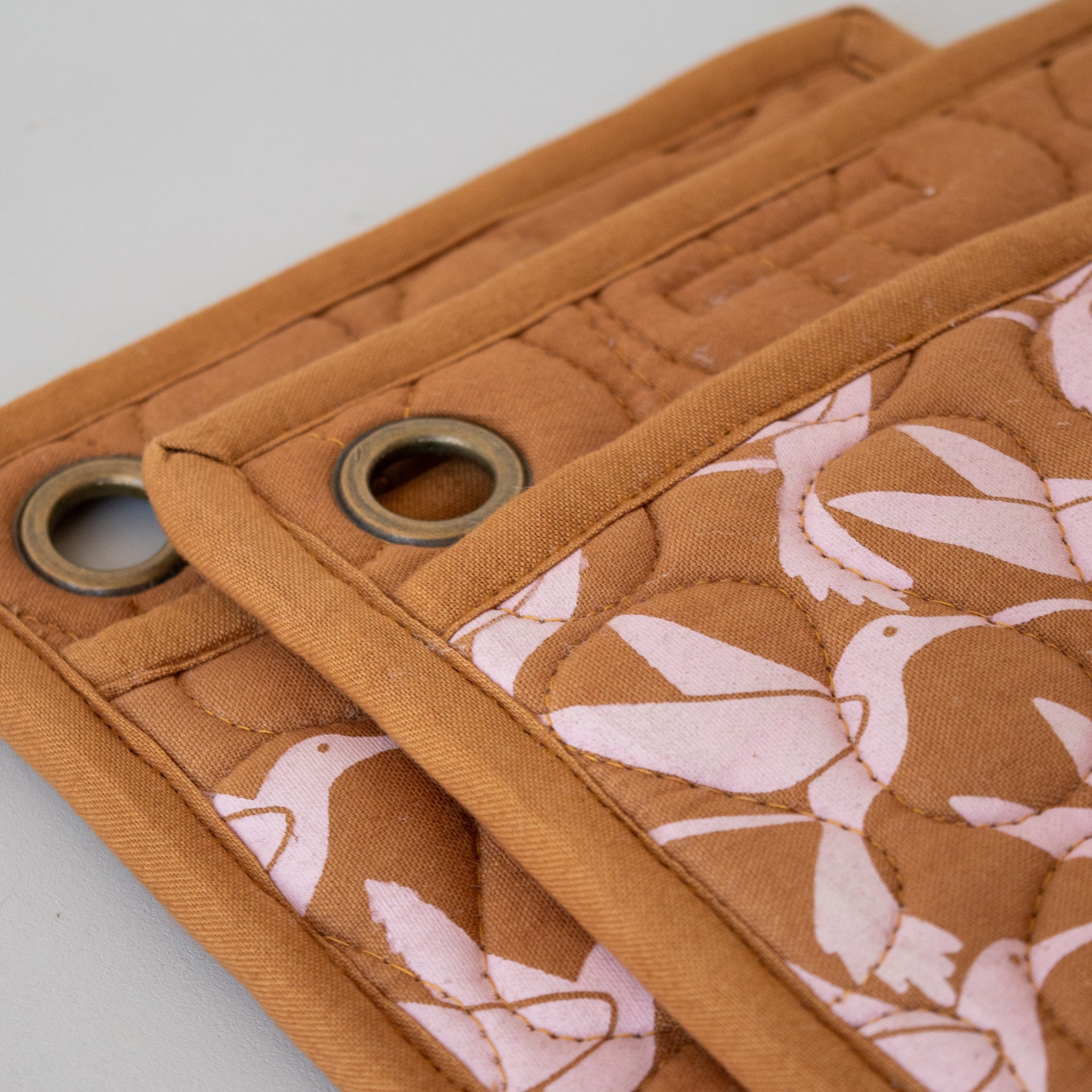 Two brown  pot holders with white bird screen print and a pocket on each, with metal loops for hanging