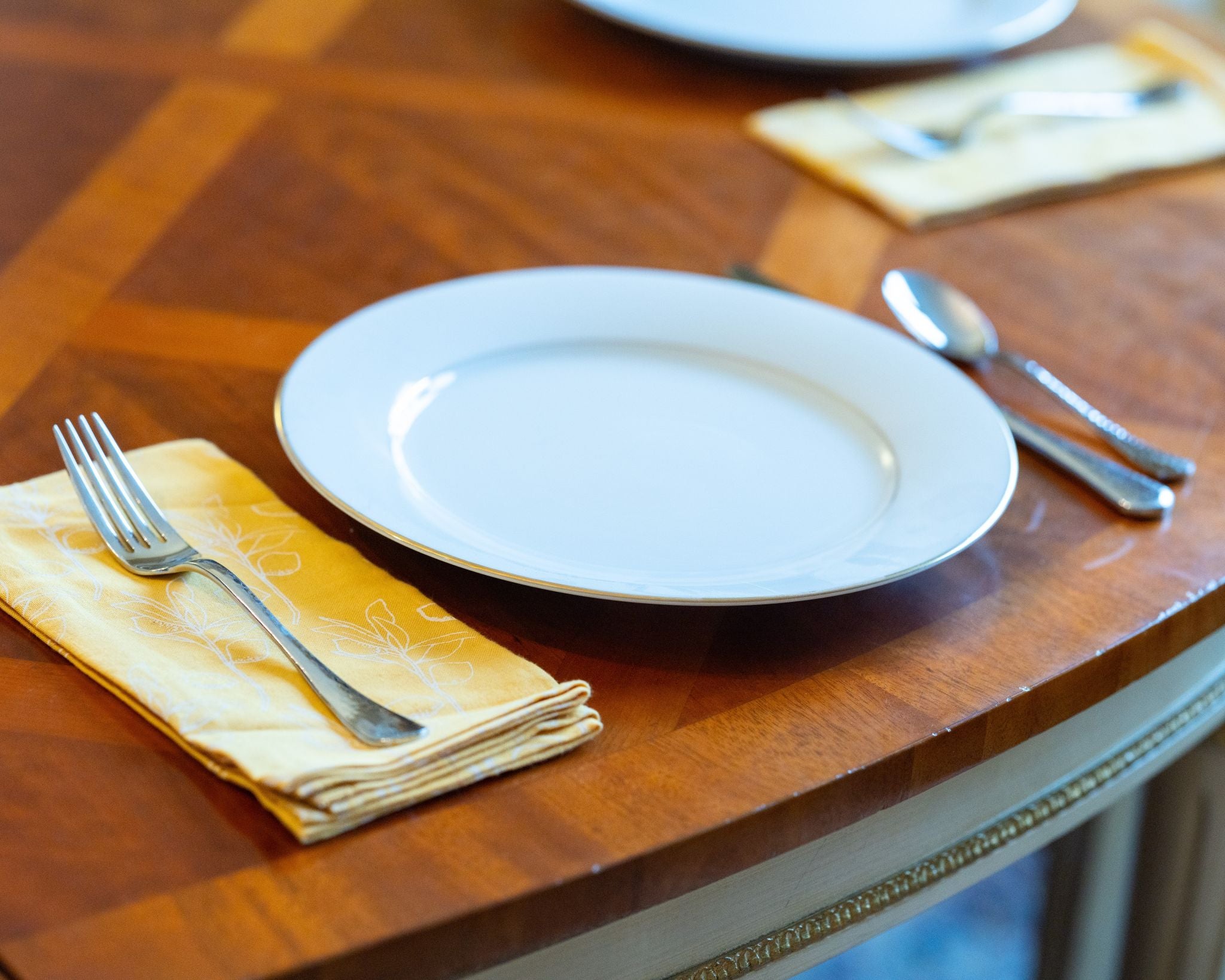 Dining table setting with a white plate, fork, and spoon on a wooden surface.