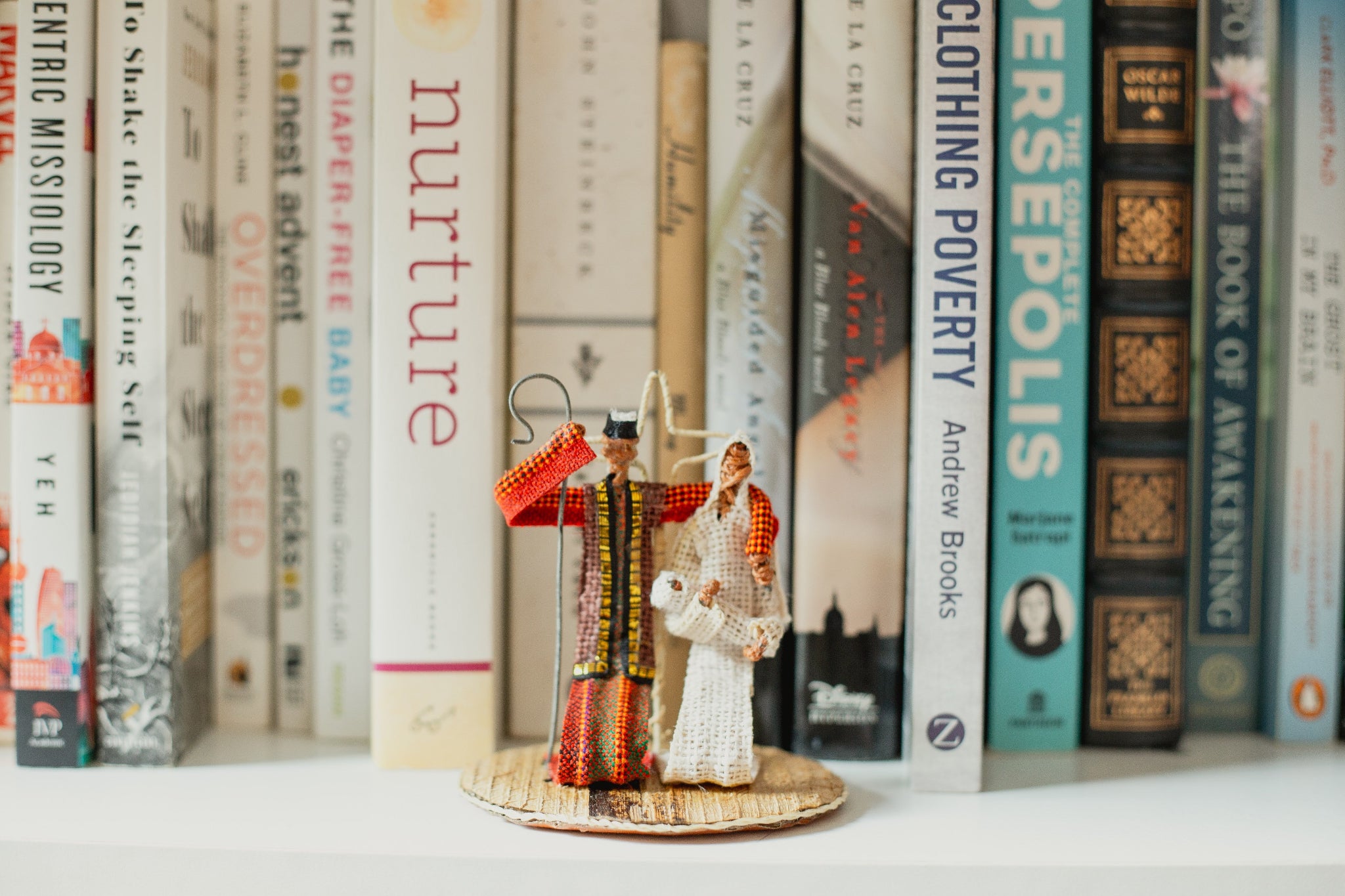 Three small figurines of the holy family on a bookshelf with books in the background.