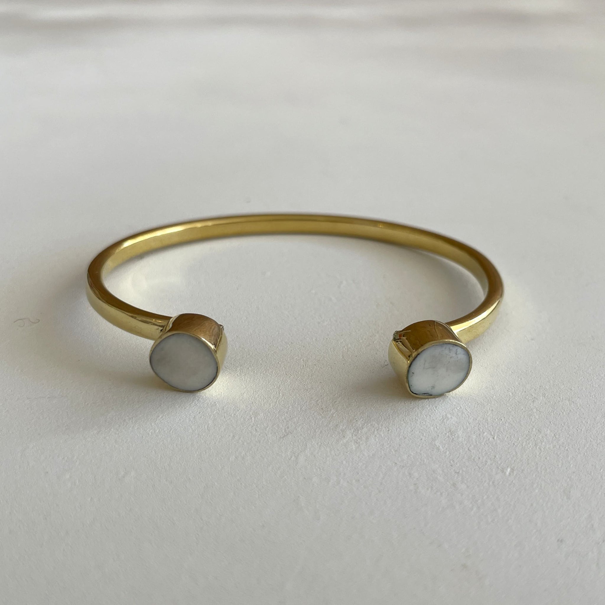 Brass bracelet with two round white bone insets on a white background