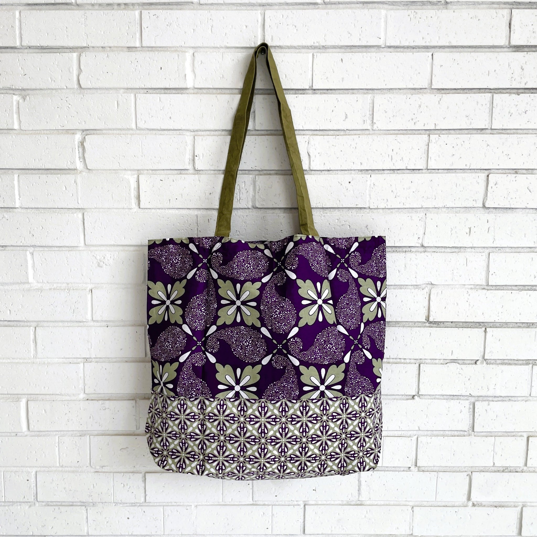 Tote bag with purple and green floral pattern against a white brick wall