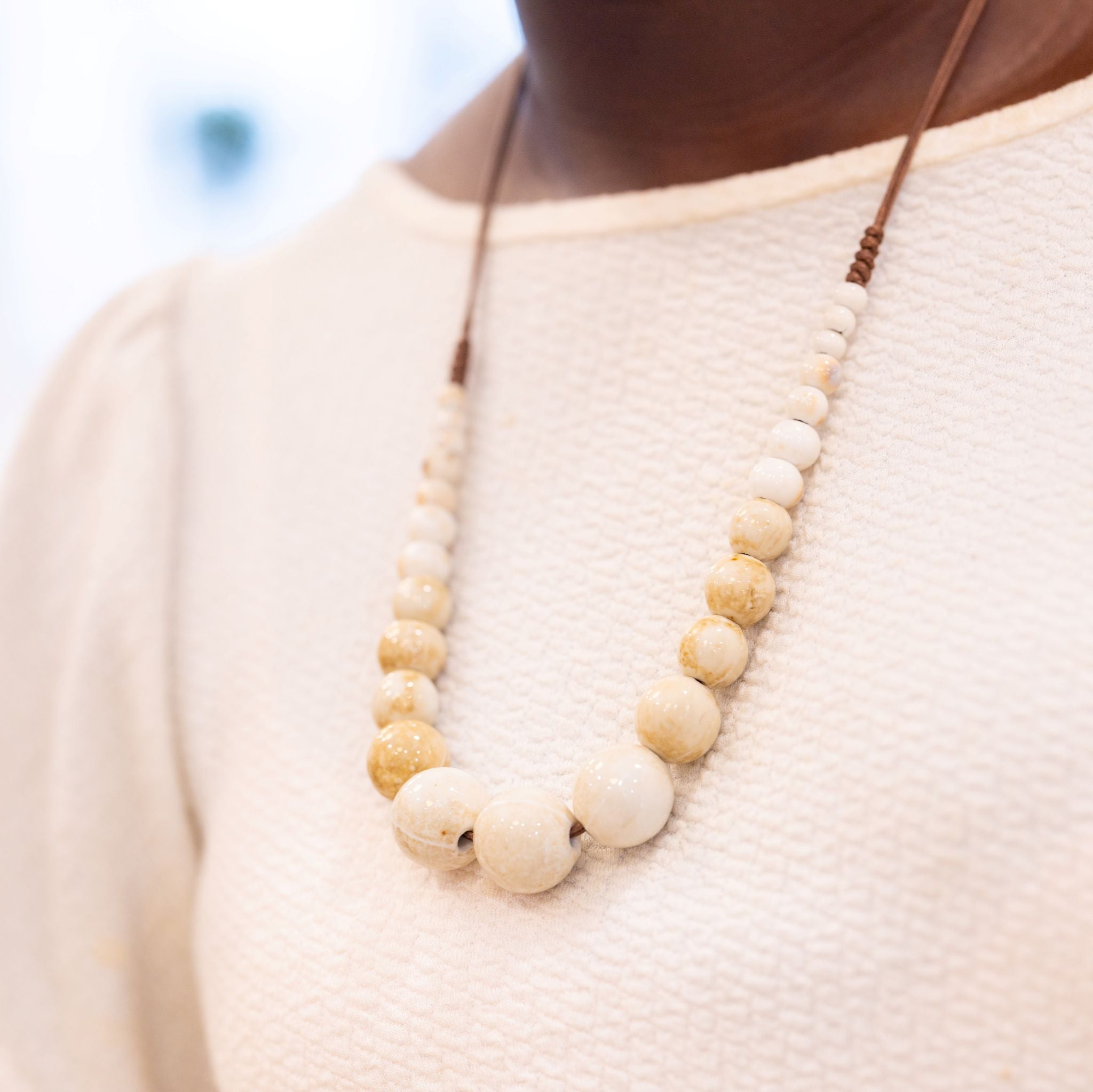 Necklace with beige beads worn by a person in a light-colored sweater.