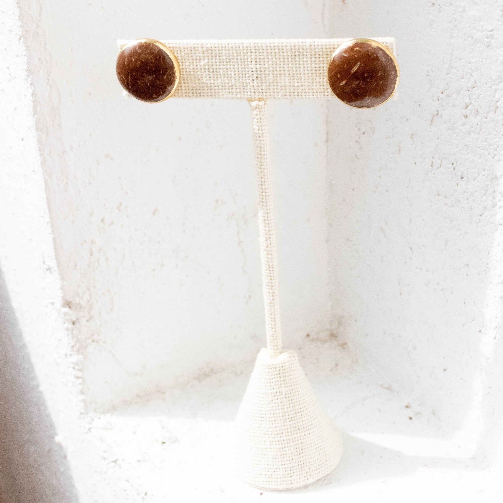 A pair of beige button-shaped coconut stud earrings displayed against a textured white background.