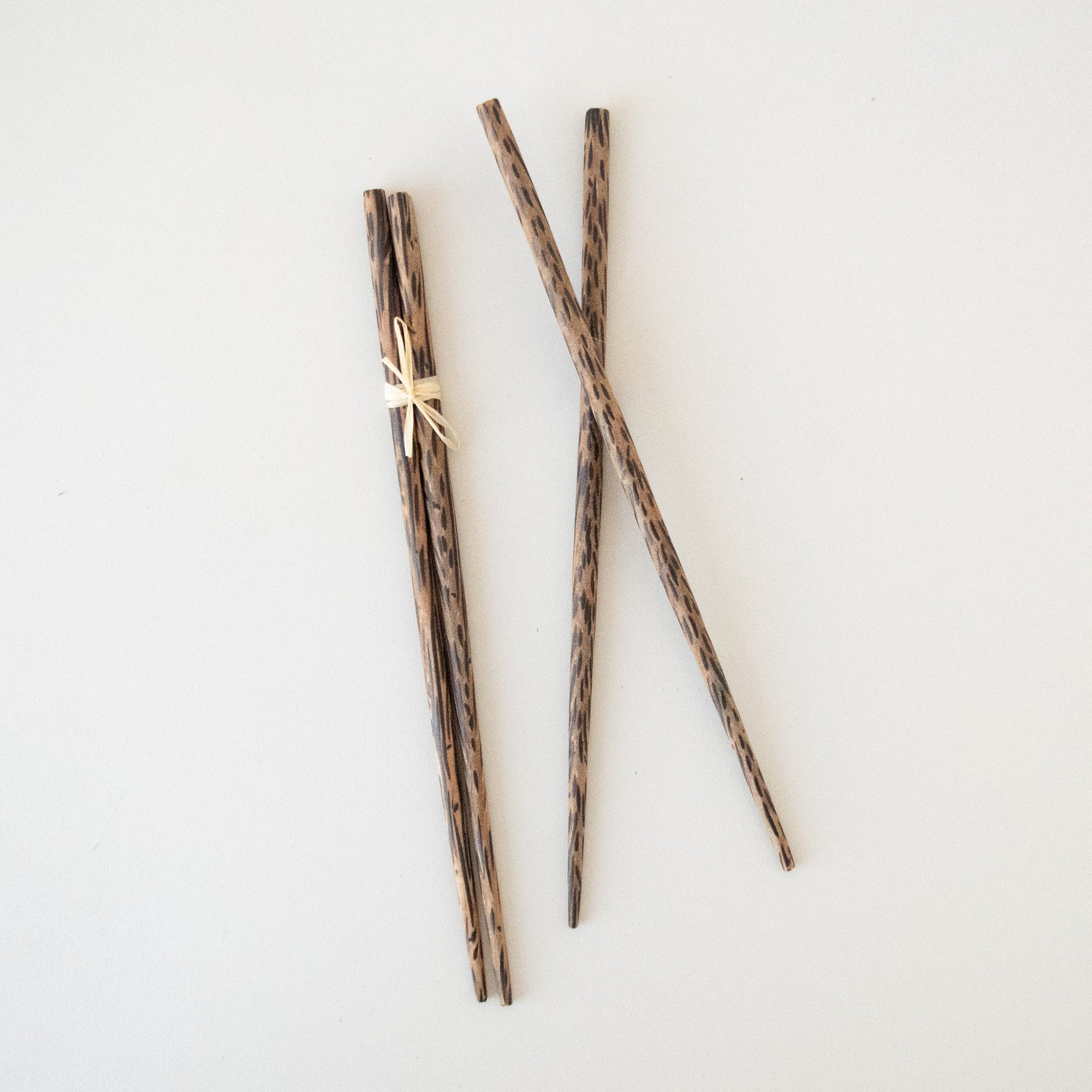 A pair of palm wood chopsticks resting on a white surface, with the texture of the wood clearly visible.