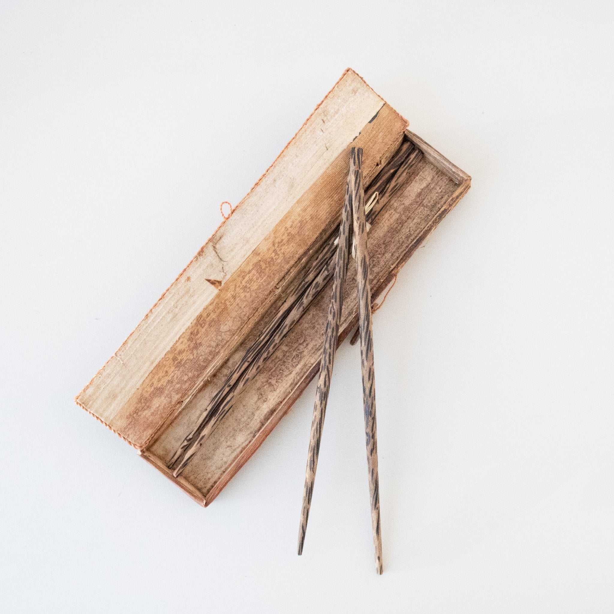 A pair of dark wood chopsticks with a natural grain pattern, resting on top of an open rectangular wooden box on a clean white background.