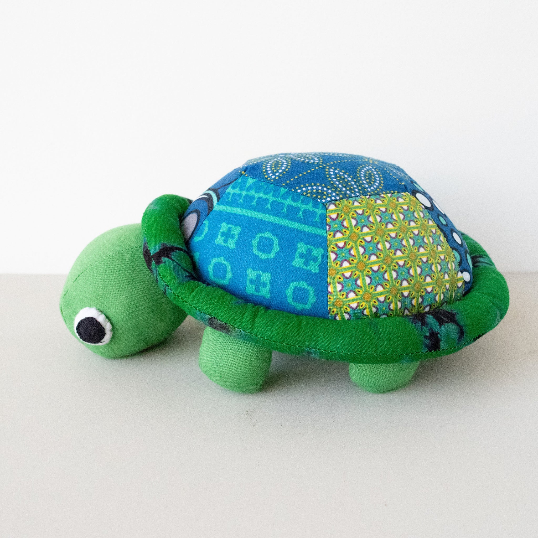 A plush toy shaped like a turtle with a green shell, blue patterns on the back, and a yellow patterned design on its side.