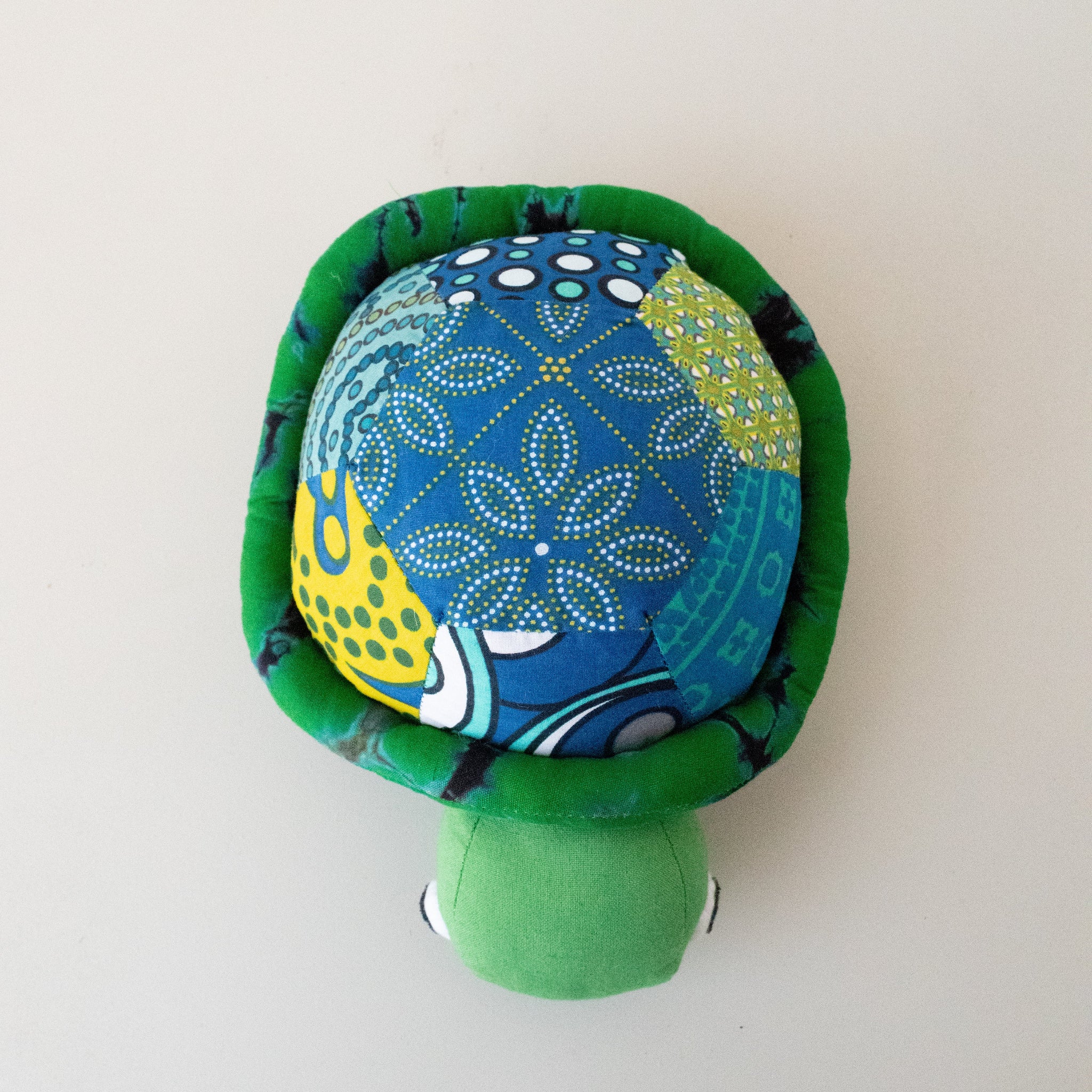 A handmade fabric turtle plush toy with a patterned blue and green shell and a solid green head, photographed against a plain off-white background.