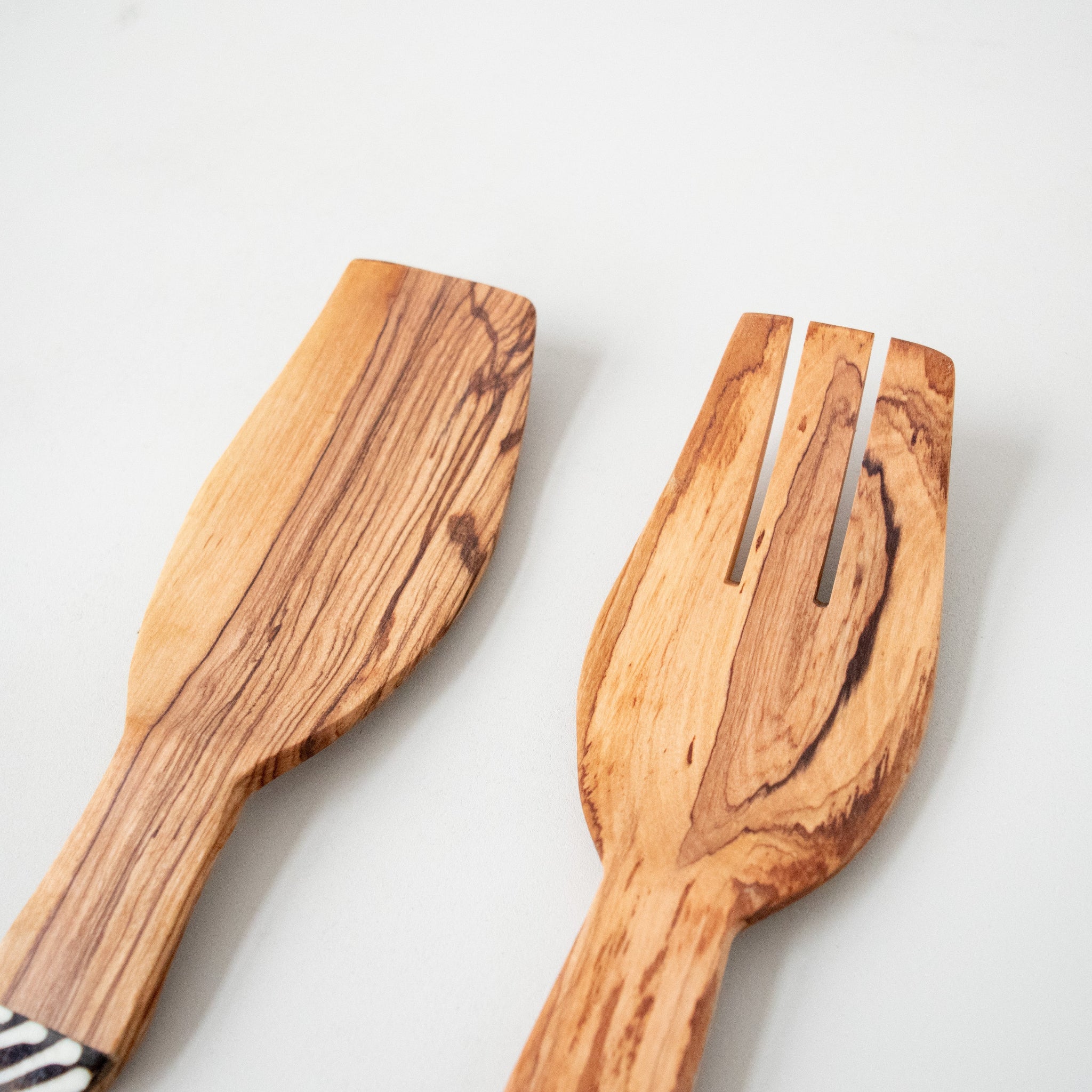 A set of two olivewood salad spoons with cow bone inlay, lying on a white surface.