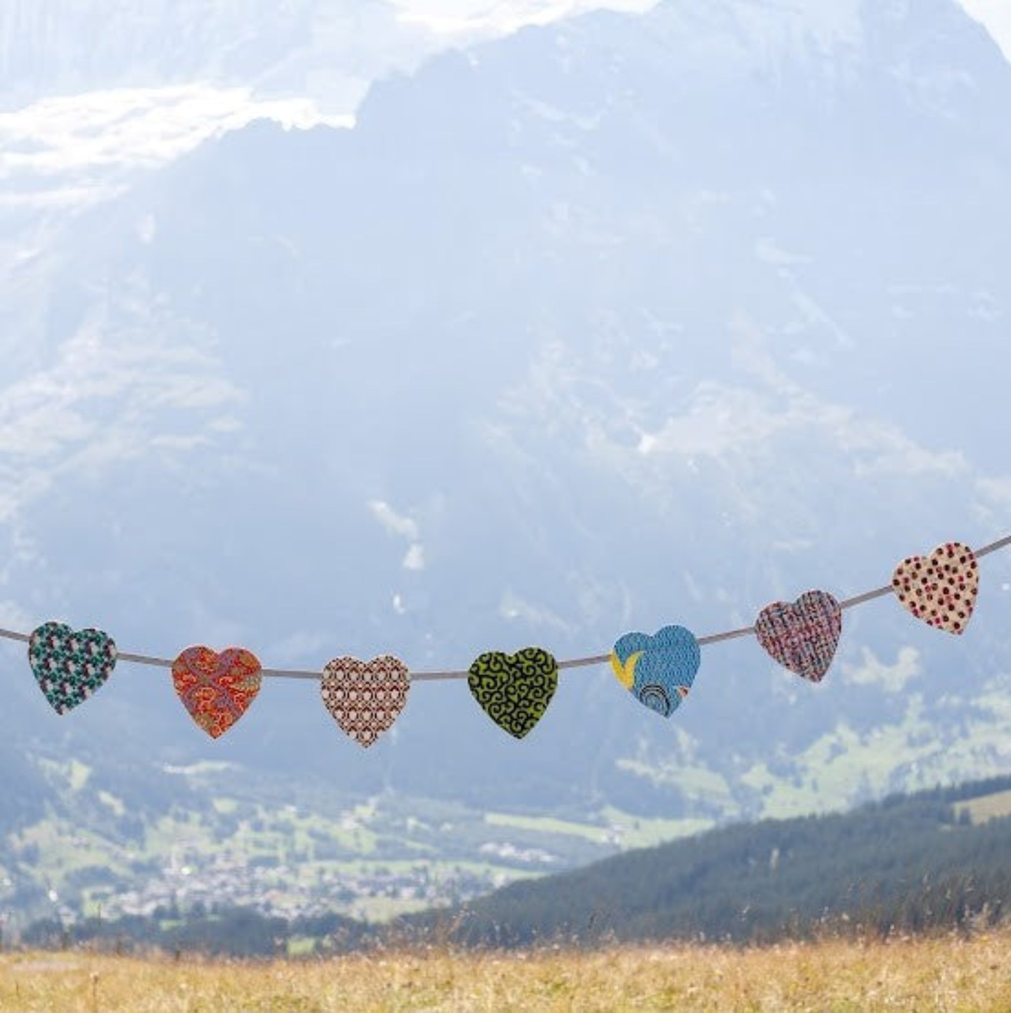 A garland of hand-sewn hearts made from various patterns of African kitenge fabric, strung across a backdrop of a mountainous landscape.