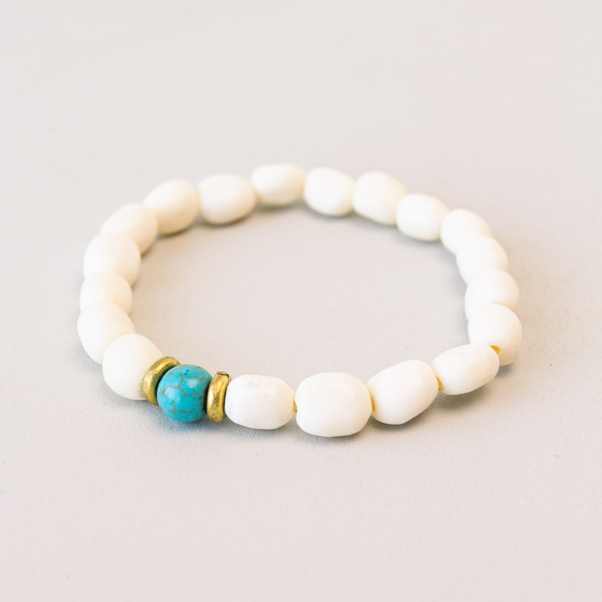 A white bone and brass bracelet with a touch of blue, displayed against a light background.