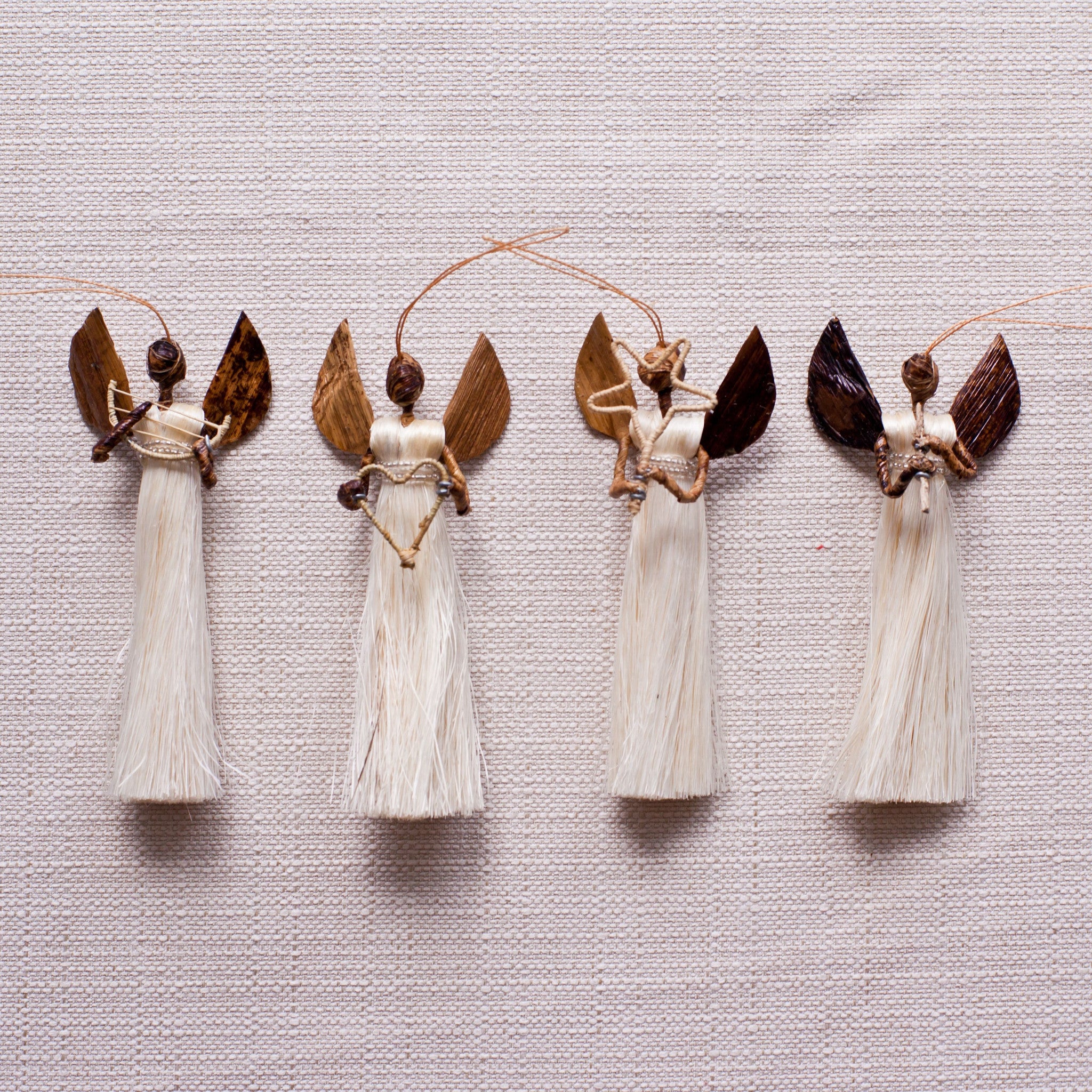 A set of four handmade sisal angel ornaments, each holding different items such as a heart, star, flute, and harp, displayed against a neutral background.