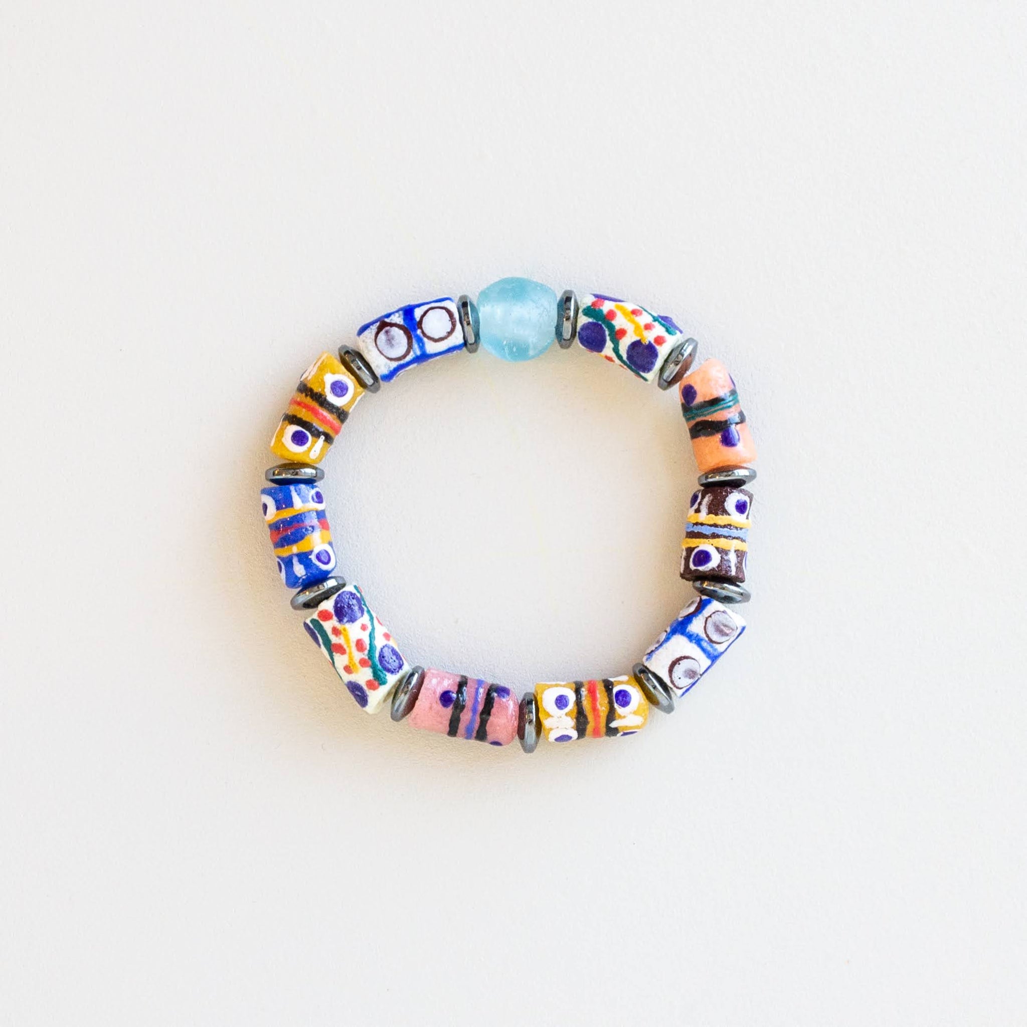 A handmade beaded stretch bracelet featuring a variety of colorful patterned glass beads and one light blue bead, displayed on a clean white background.